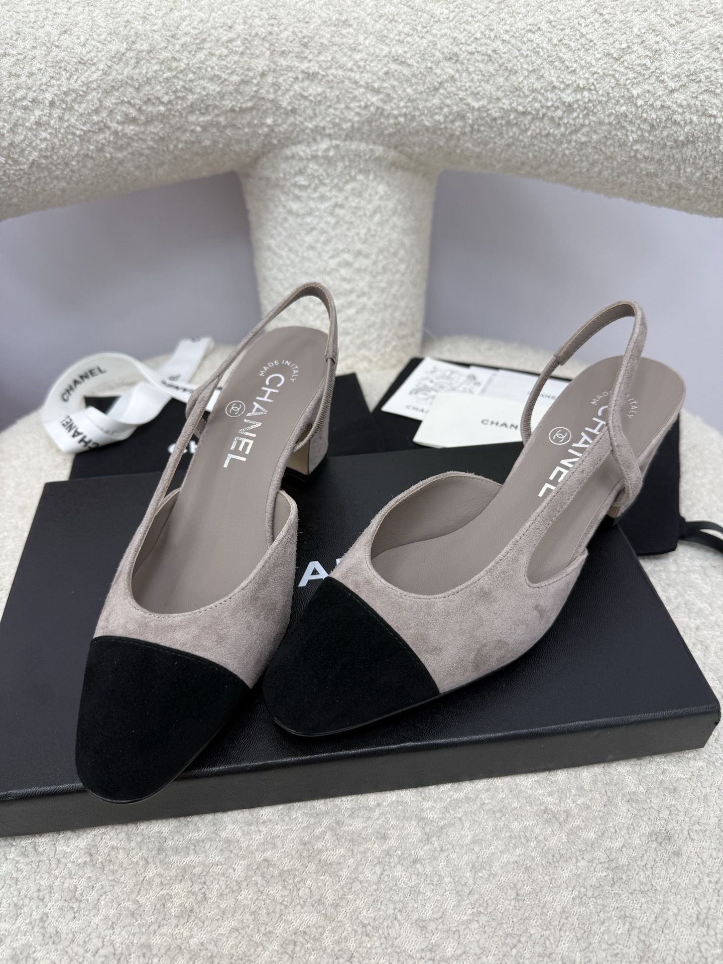 Chanel grey suede slingback pumps with black cap toe and block heel displayed on a white textured chair - Hình 6