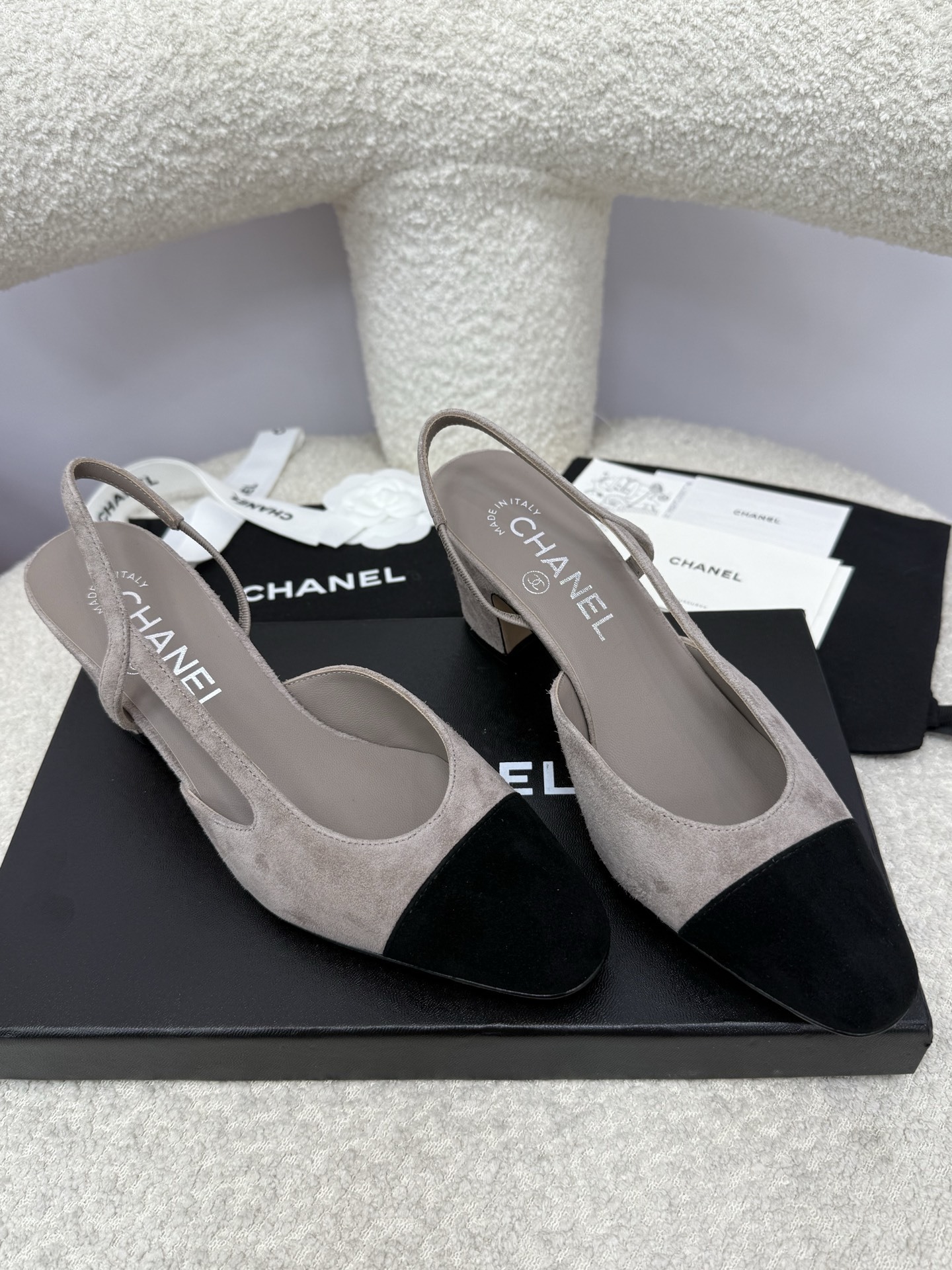 Chanel grey suede slingback pumps with black cap toe and block heel displayed on a white textured chair - Hình 5