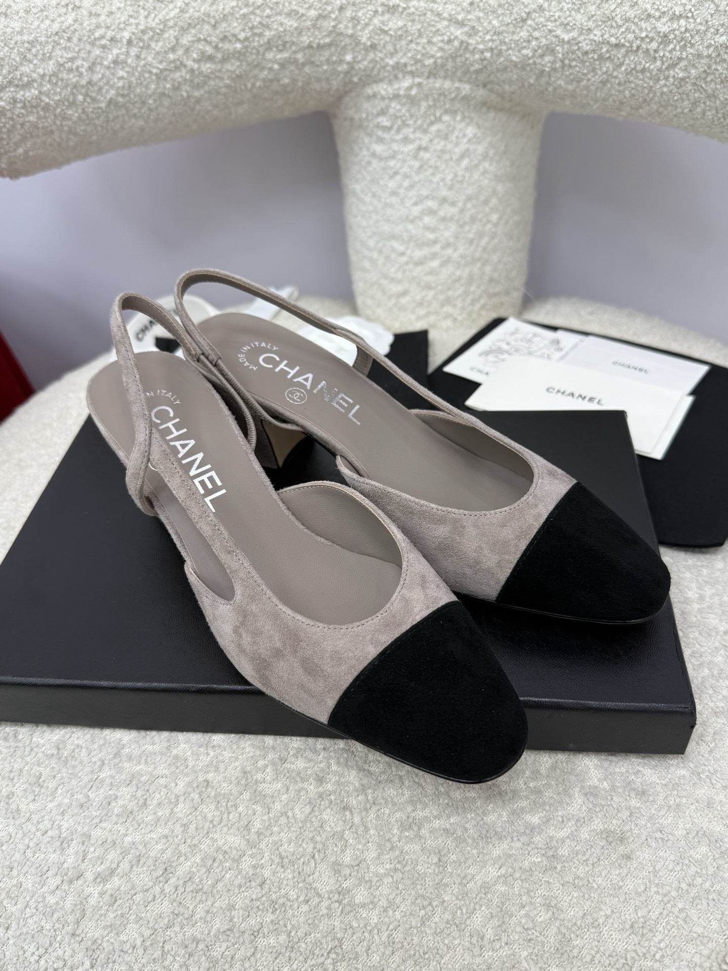 Chanel grey suede slingback pumps with black cap toe and block heel displayed on a white textured chair - Hình 4