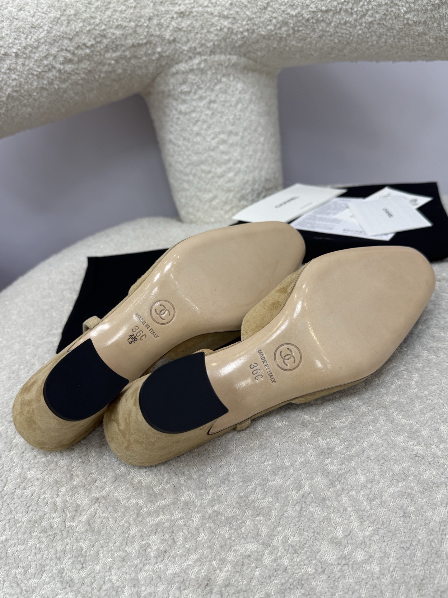 A pair of luxury Chanel beige suede slingback pumps with black cap toes and block heels on a white textured surface. - Hình 9