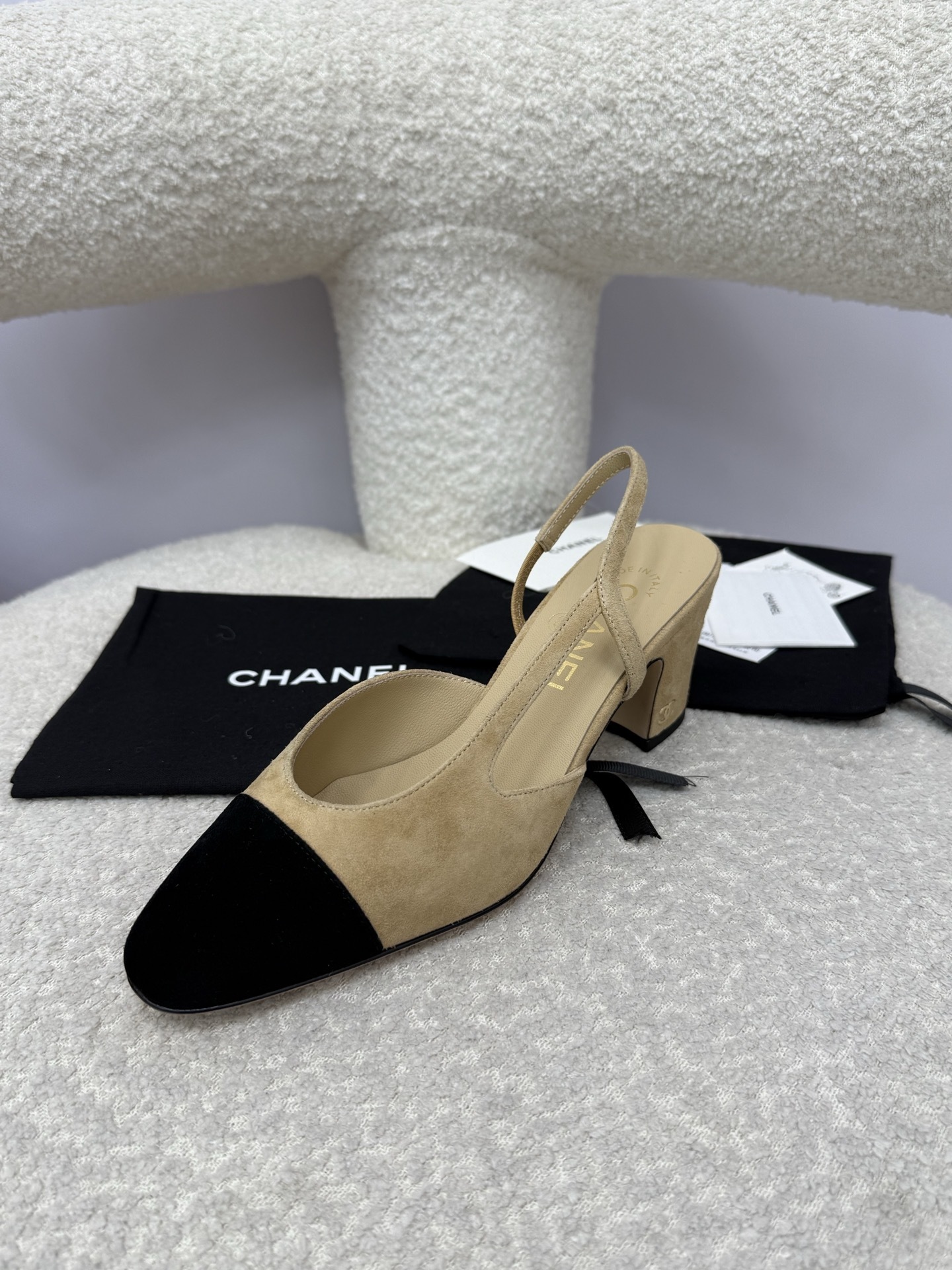 A pair of luxury Chanel beige suede slingback pumps with black cap toes and block heels on a white textured surface. - Hình 3