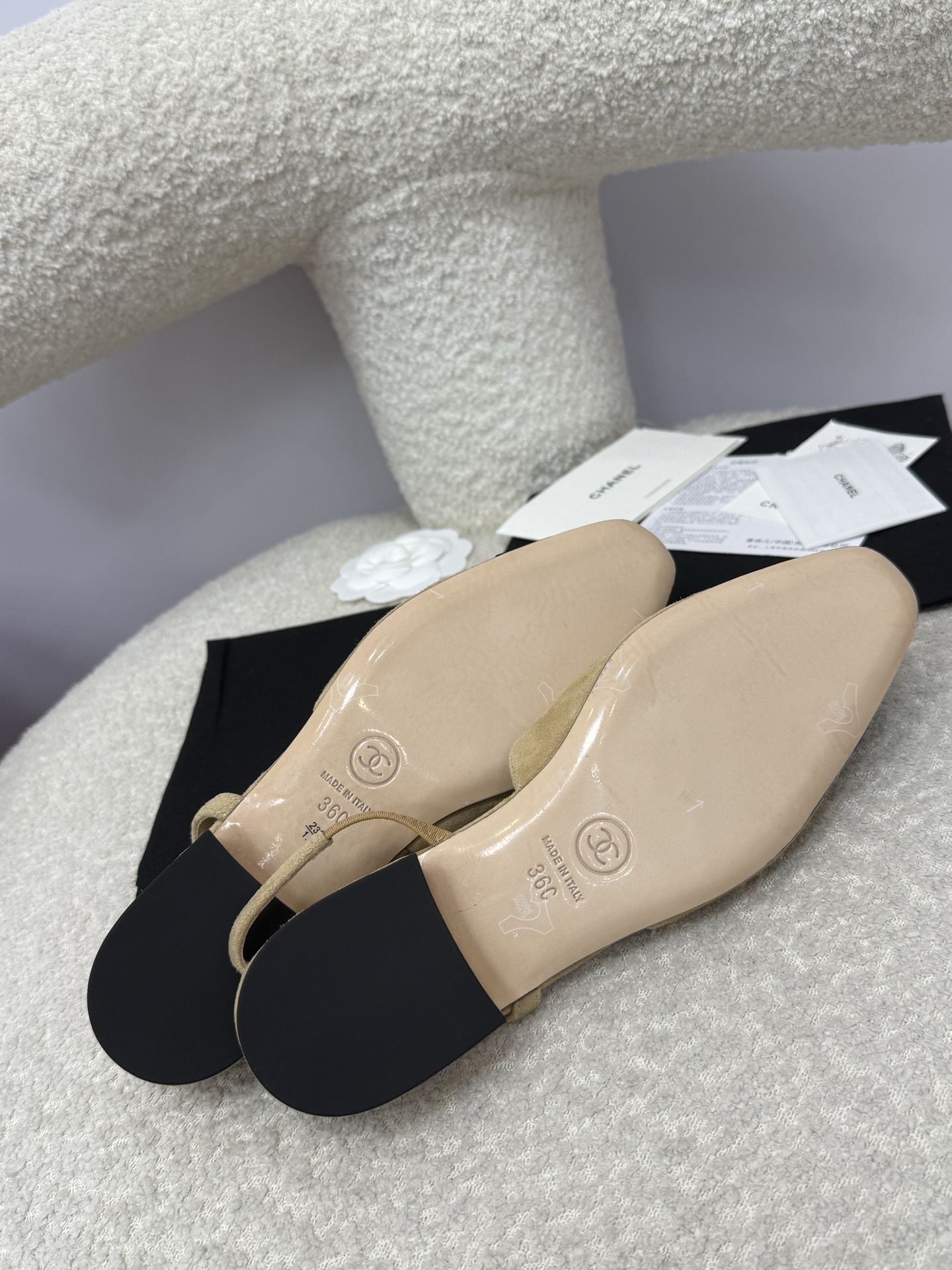 A pair of Chanel two-tone beige and black suede slingback flats displayed on a white textured surface with branded dust bags and authentication cards. - Hình 9