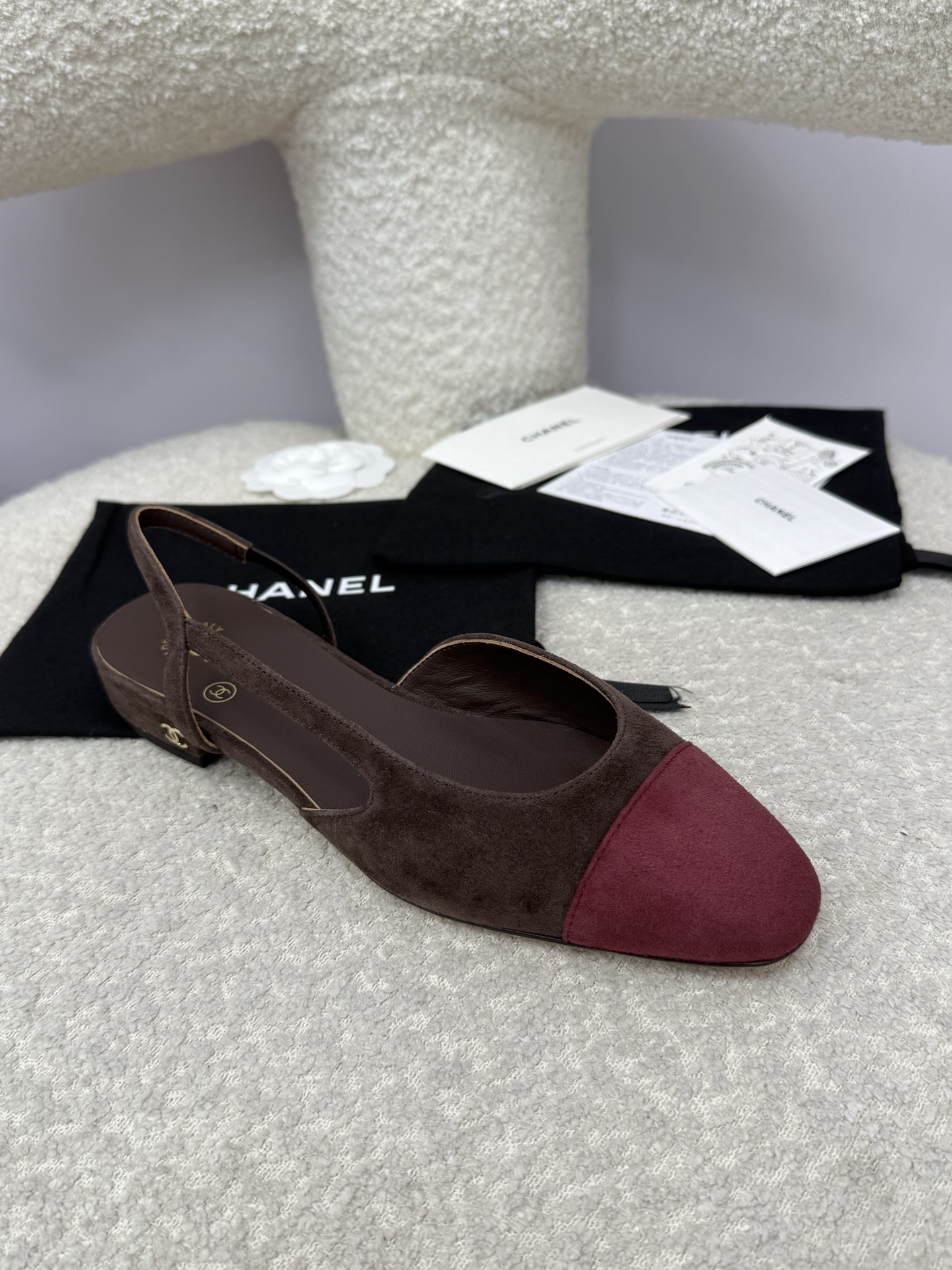 Pair of Chanel two-tone slingback flats in brown suede with burgundy cap toe on a white textured surface with packaging. - Hình 2