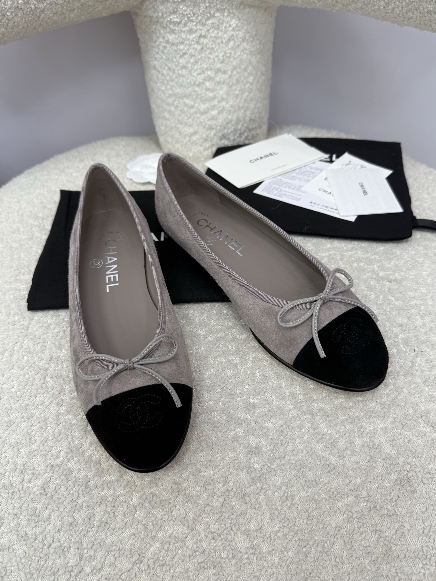 Pair of Chanel grey suede ballerina flats with black suede cap-toe and bow detail on a white textured surface. - Hình 9