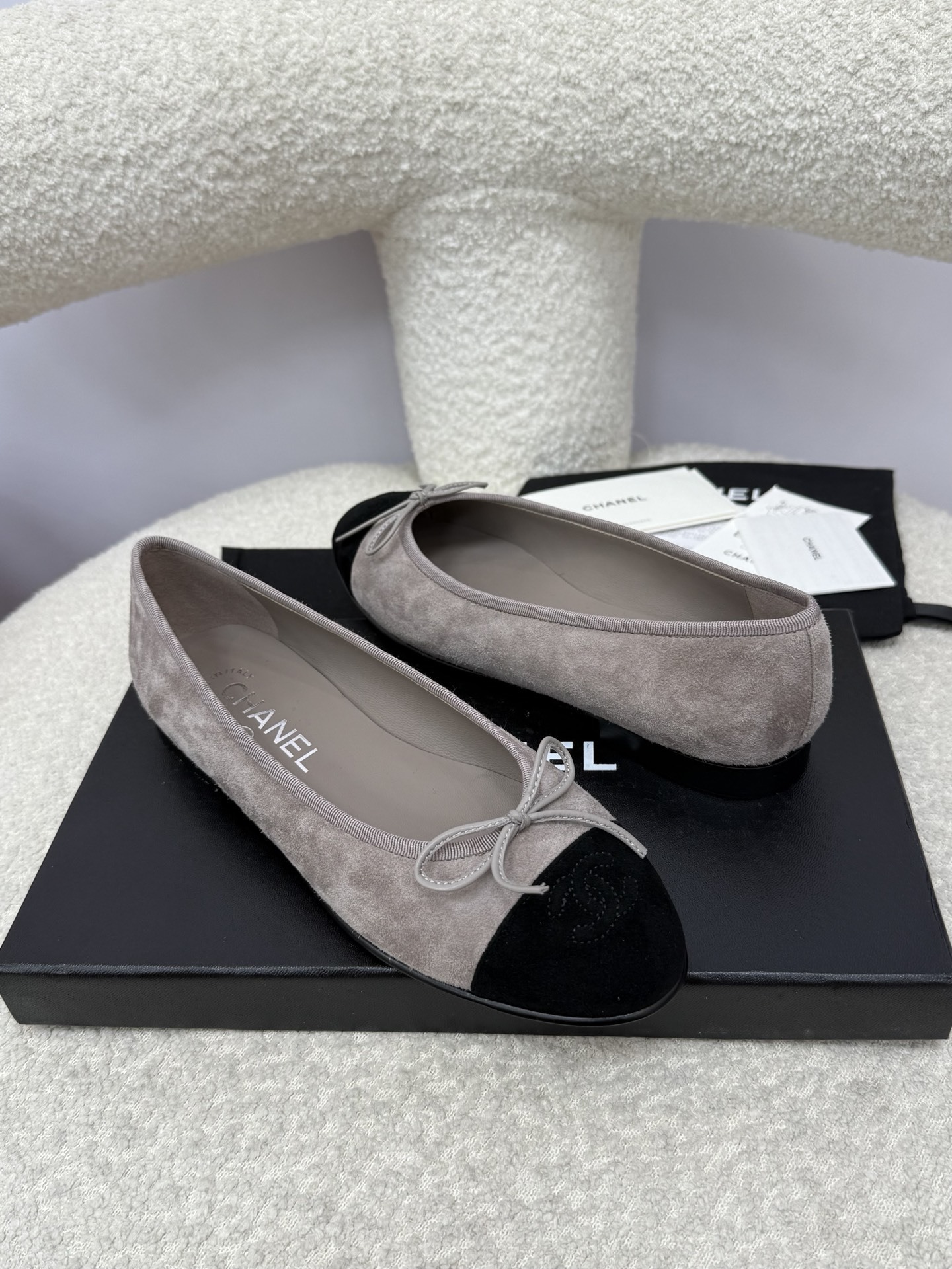 Pair of Chanel grey suede ballerina flats with black suede cap-toe and bow detail on a white textured surface. - Hình 6