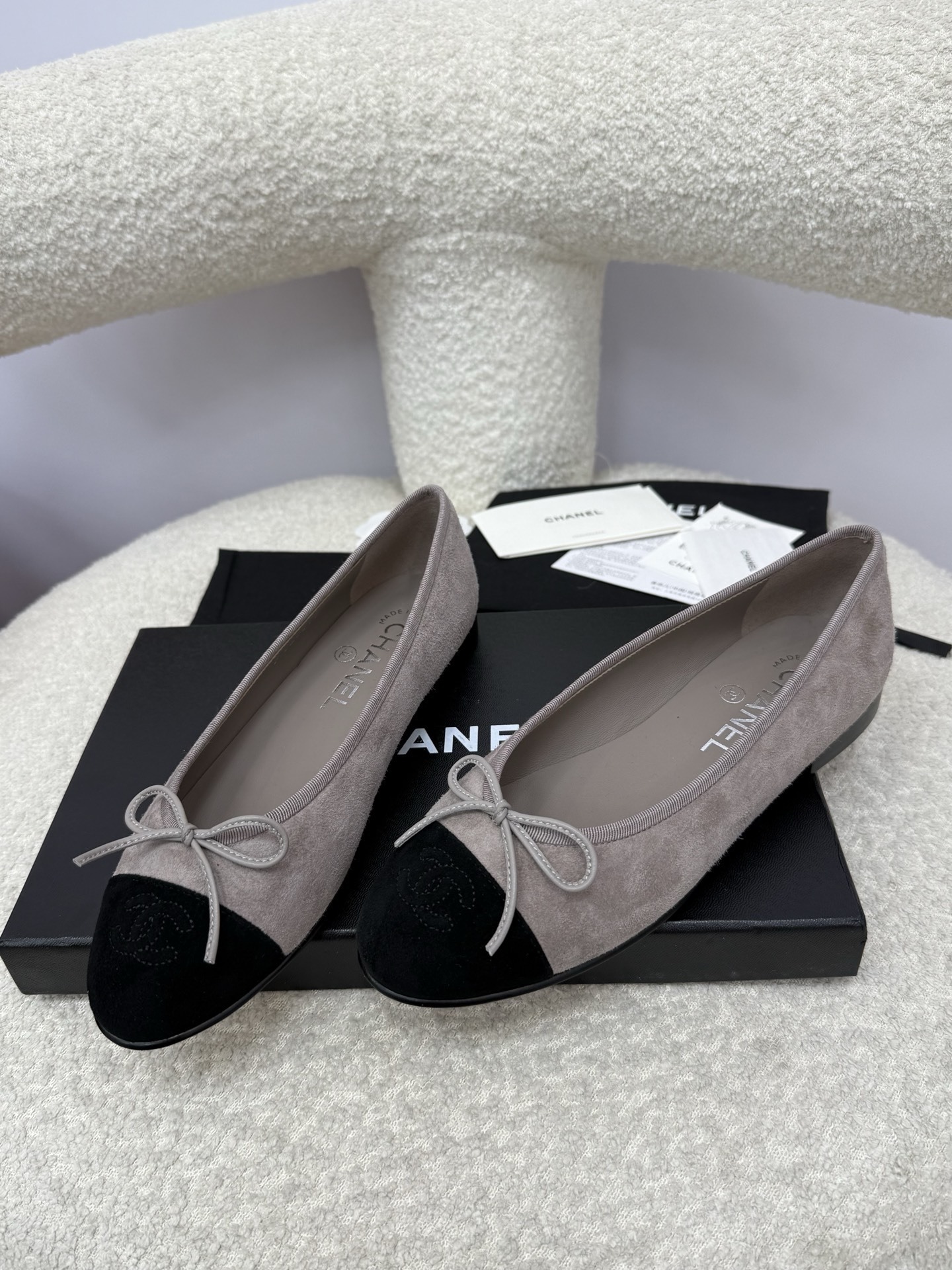 Pair of Chanel grey suede ballerina flats with black suede cap-toe and bow detail on a white textured surface. - Hình 5