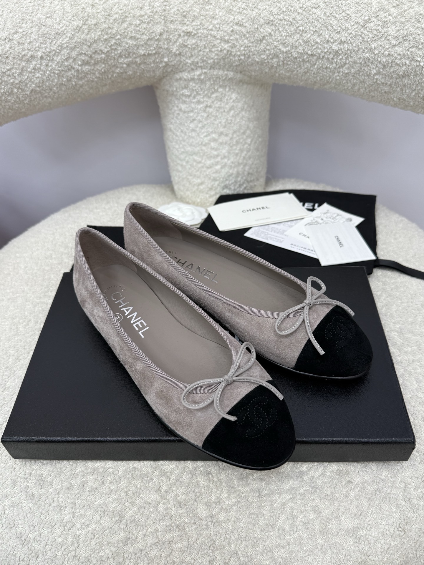 Pair of Chanel grey suede ballerina flats with black suede cap-toe and bow detail on a white textured surface. - Hình 4