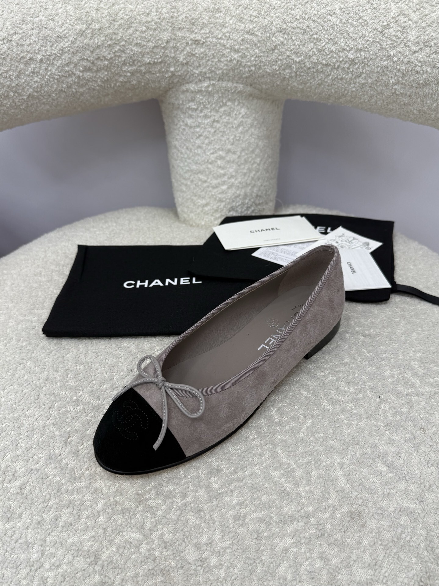 Pair of Chanel grey suede ballerina flats with black suede cap-toe and bow detail on a white textured surface. - Hình 3