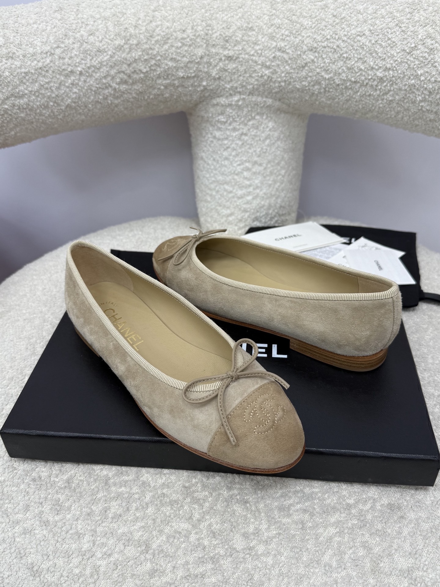 Pair of beige Chanel suede ballerina flats with CC logo toe cap and bow detail on a white textured surface - Hình 6