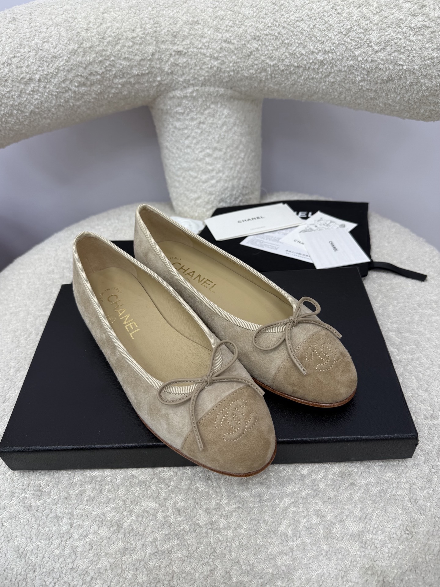Pair of beige Chanel suede ballerina flats with CC logo toe cap and bow detail on a white textured surface - Hình 4