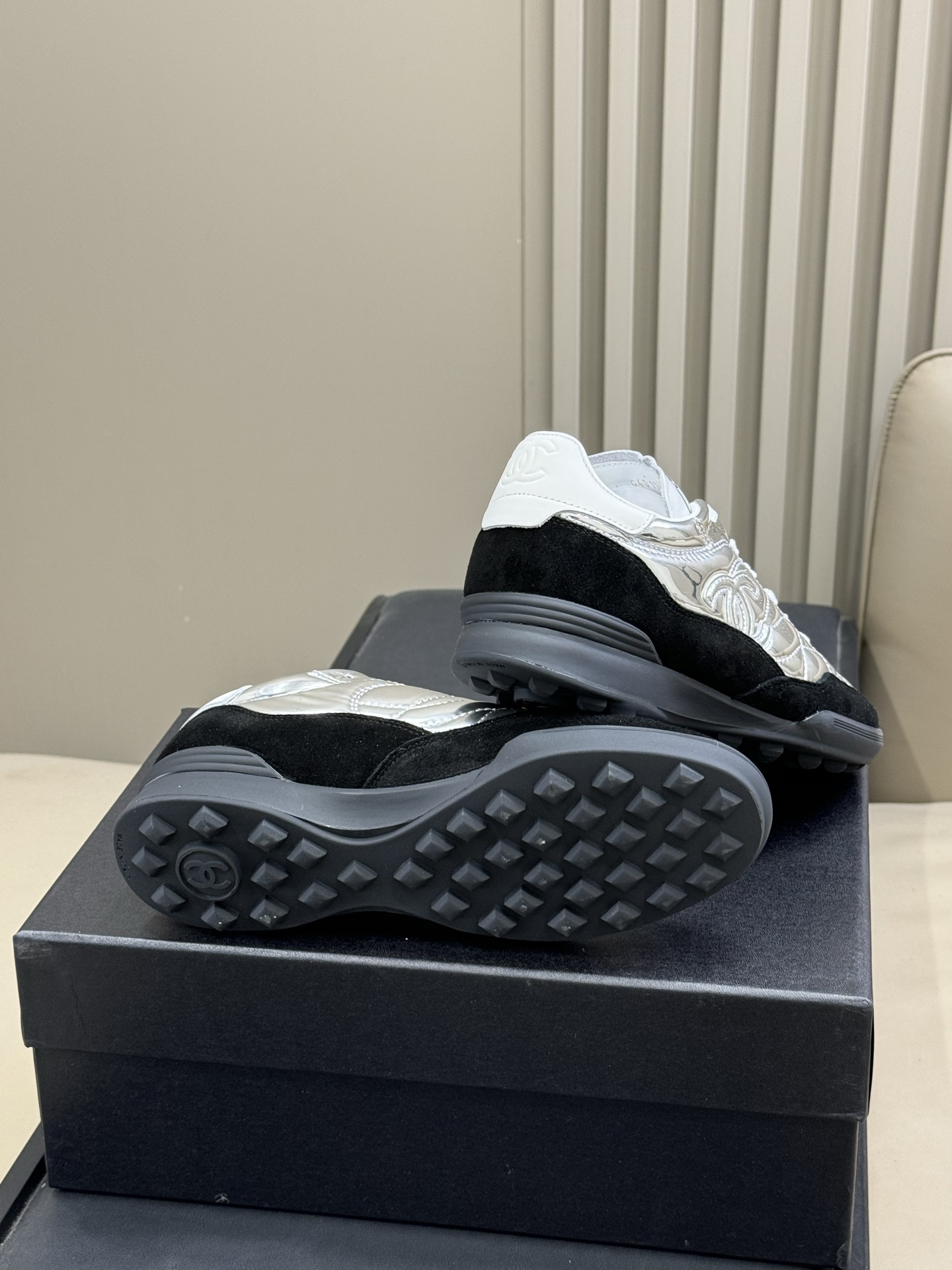 Chanel low-top sneakers with silver metallic quilted upper and black suede trim displayed on a black designer box. - Hình 9