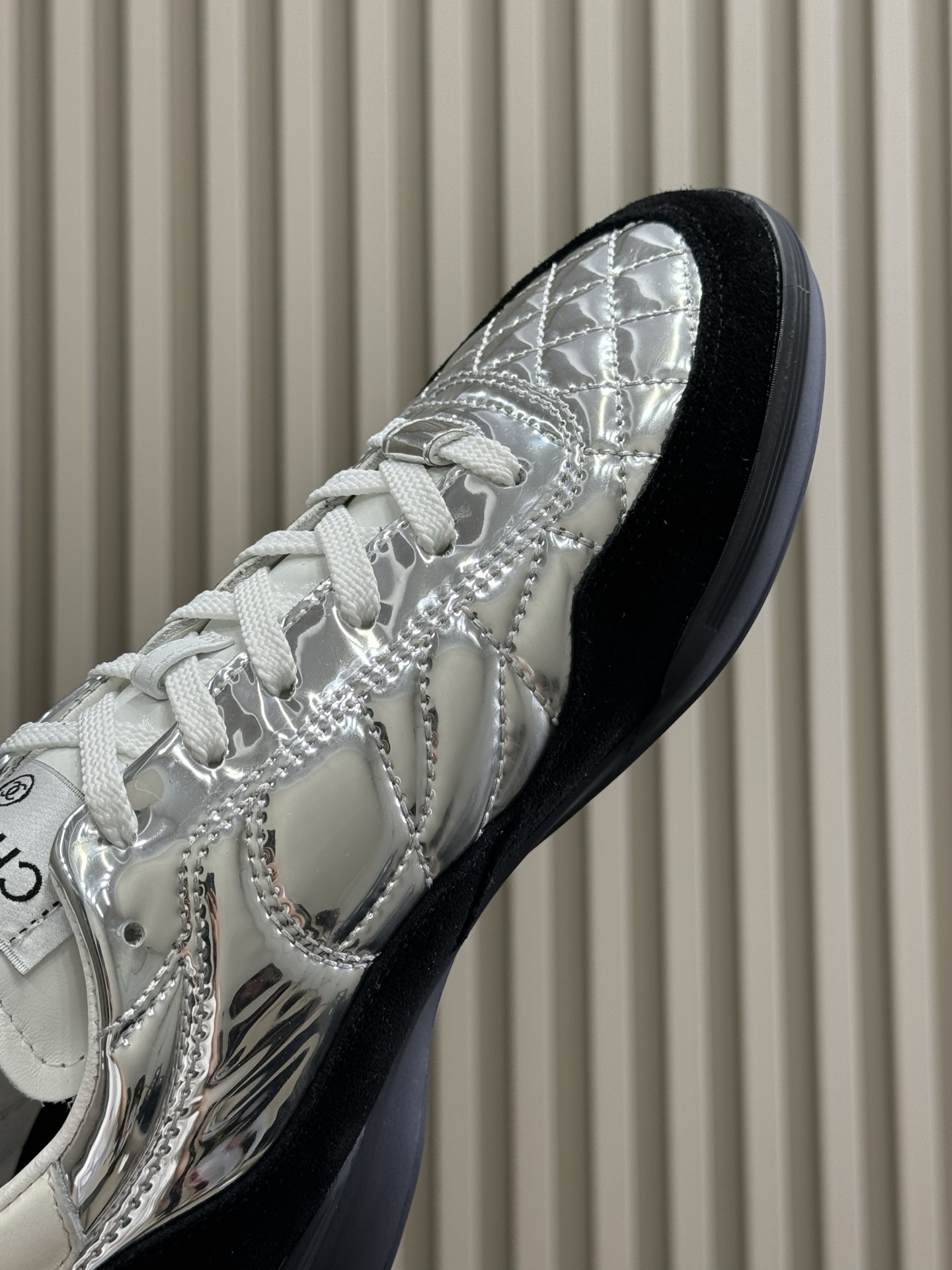 Chanel low-top sneakers with silver metallic quilted upper and black suede trim displayed on a black designer box. - Hình 7
