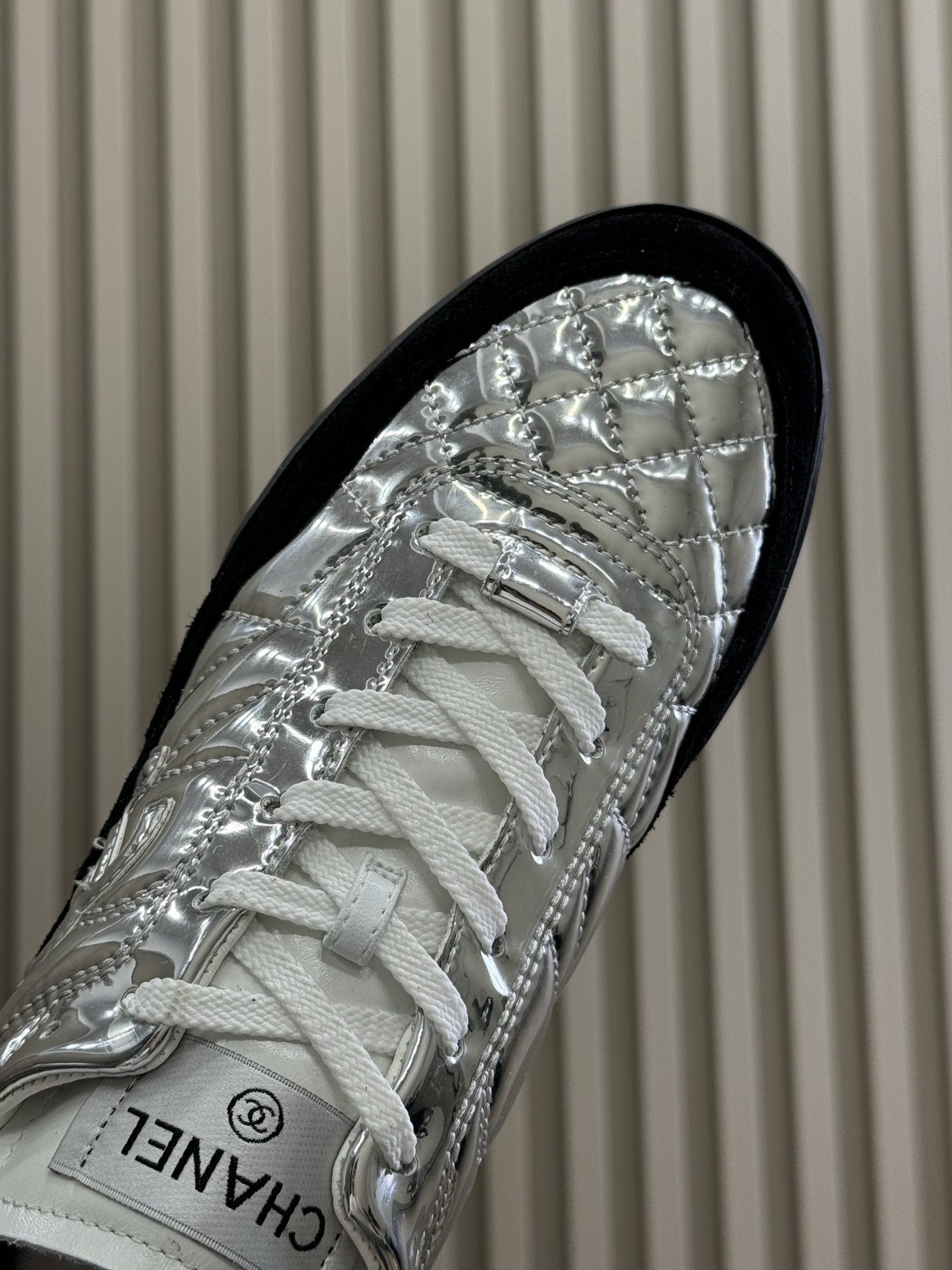 Chanel low-top sneakers with silver metallic quilted upper and black suede trim displayed on a black designer box. - Hình 6