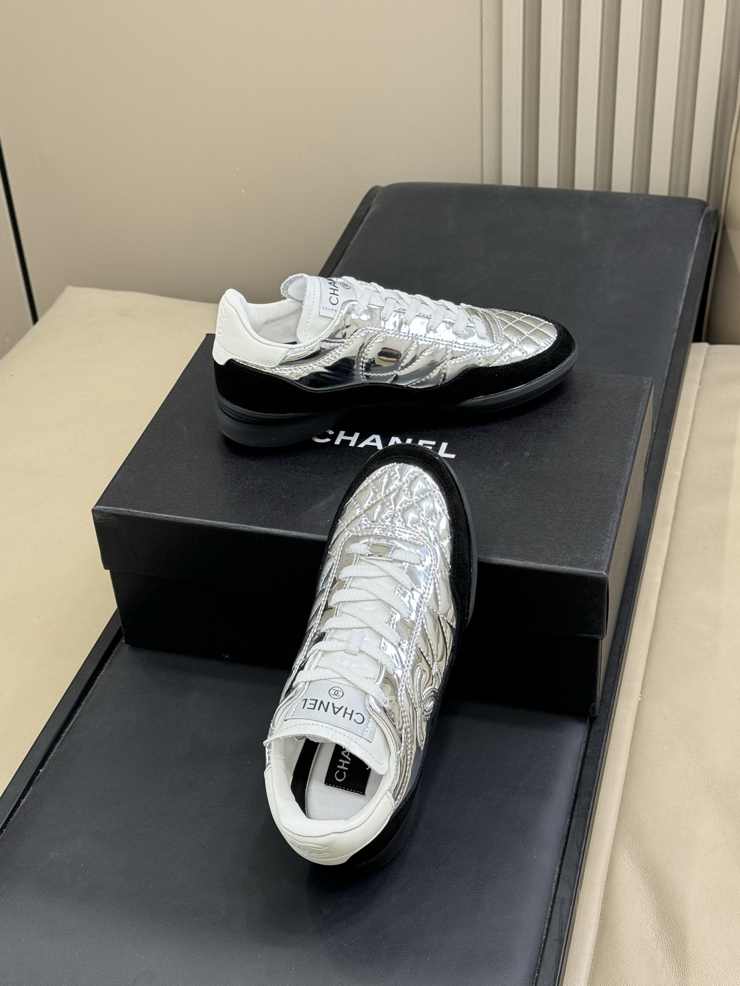 Chanel low-top sneakers with silver metallic quilted upper and black suede trim displayed on a black designer box. - Hình 5