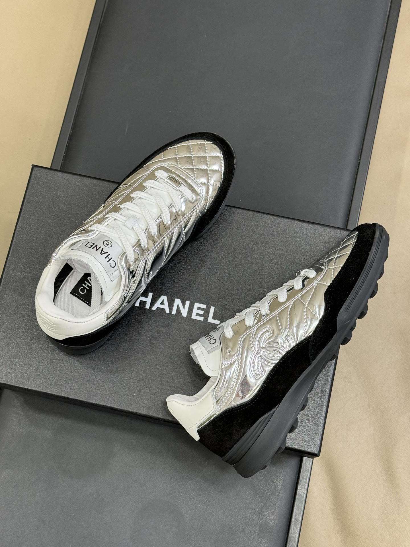 Chanel low-top sneakers with silver metallic quilted upper and black suede trim displayed on a black designer box. - Hình 4