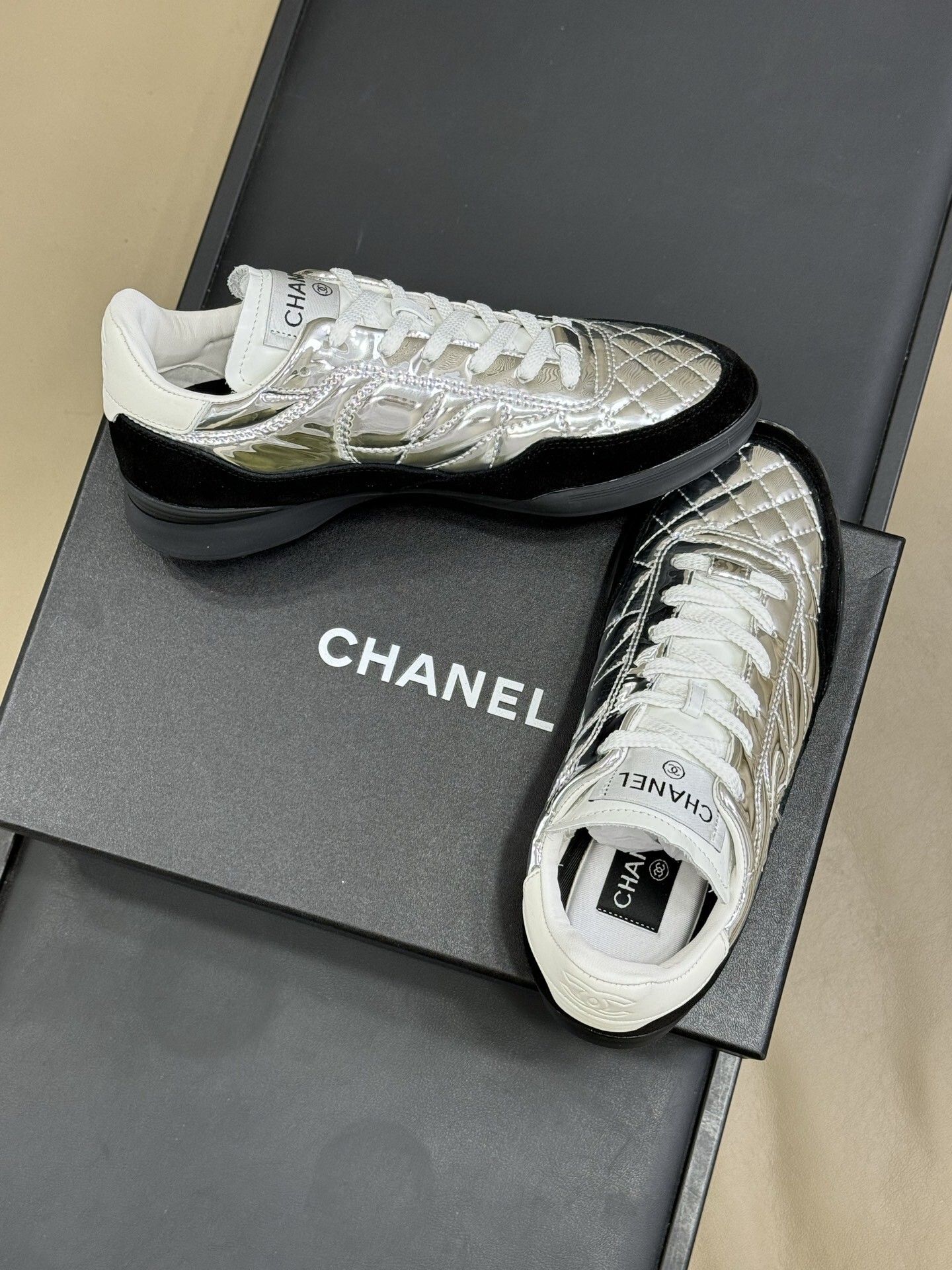 Chanel low-top sneakers with silver metallic quilted upper and black suede trim displayed on a black designer box. - Hình 3