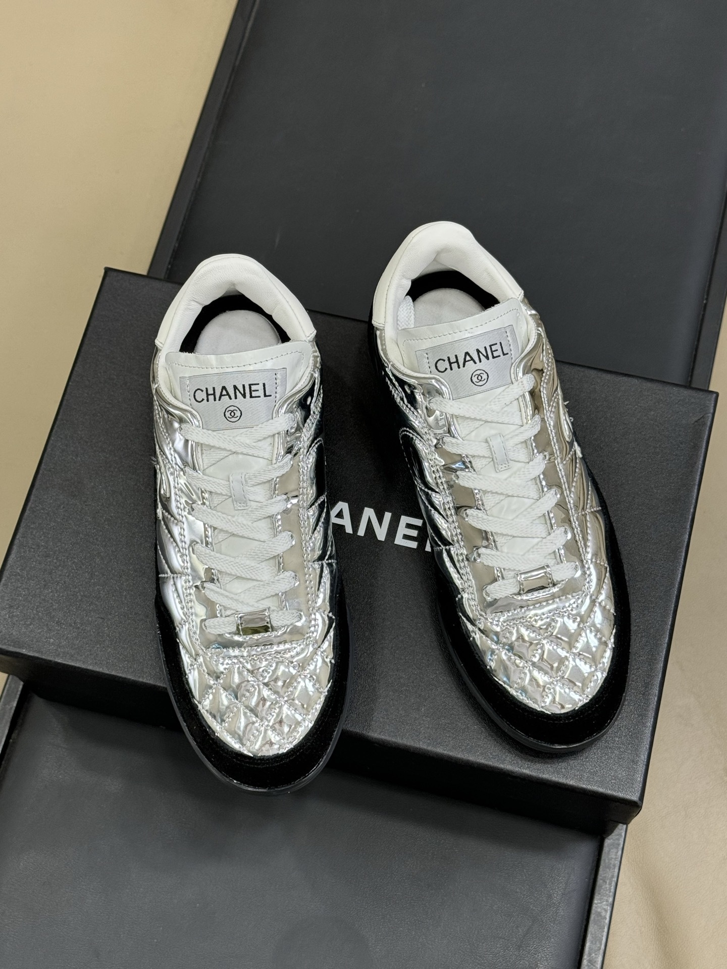 Chanel low-top sneakers with silver metallic quilted upper and black suede trim displayed on a black designer box. - Hình 2