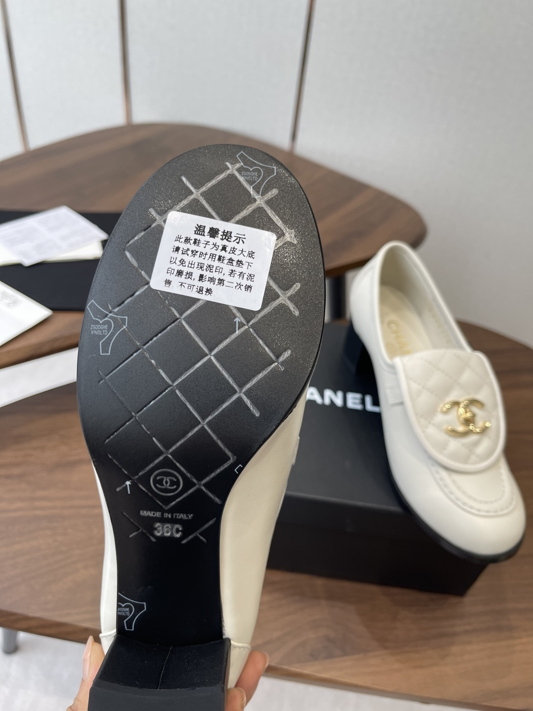 Chanel off-white quilted leather loafers with gold CC logo and black block heel on a wooden table - Hình 9