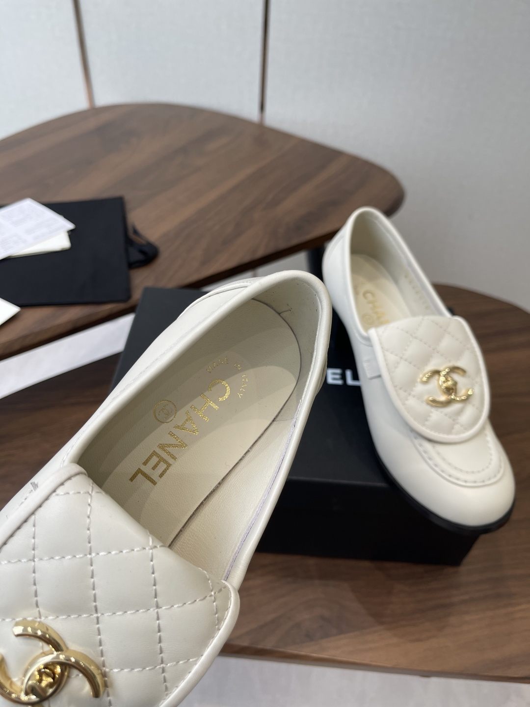 Chanel off-white quilted leather loafers with gold CC logo and black block heel on a wooden table - Hình 7