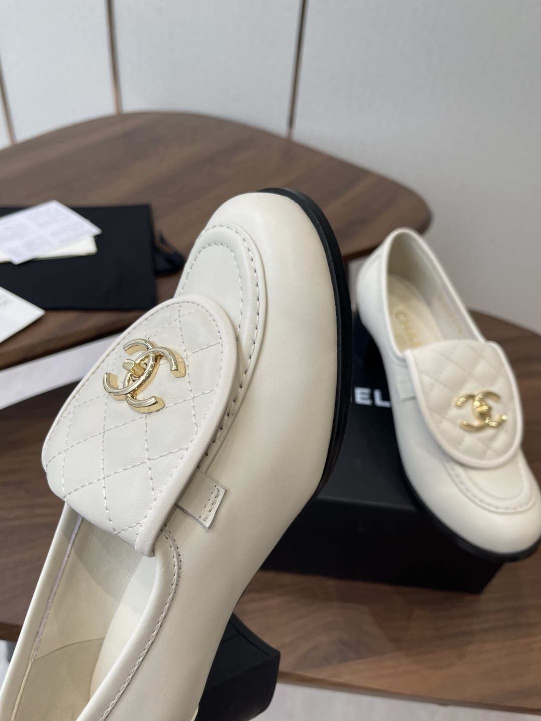 Chanel off-white quilted leather loafers with gold CC logo and black block heel on a wooden table - Hình 6