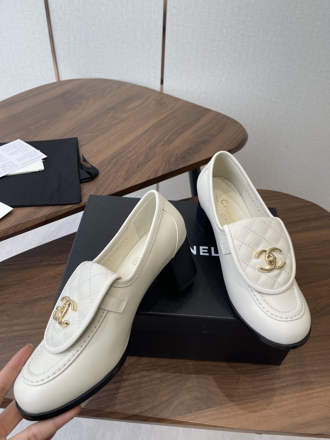 Chanel off-white quilted leather loafers with gold CC logo and black block heel on a wooden table - Hình 5