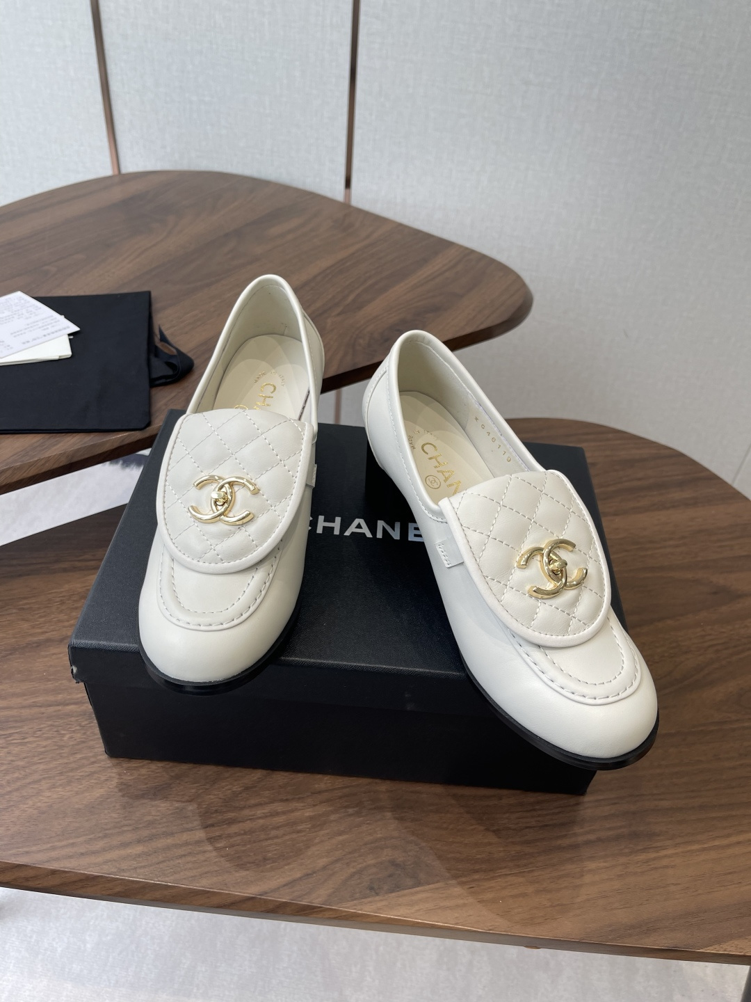 Chanel off-white quilted leather loafers with gold CC logo and black block heel on a wooden table - Hình 4