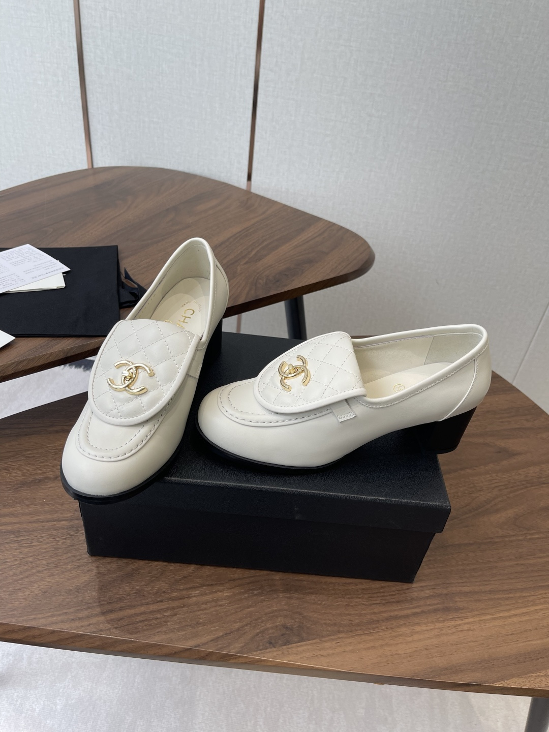 Chanel off-white quilted leather loafers with gold CC logo and black block heel on a wooden table - Hình 3
