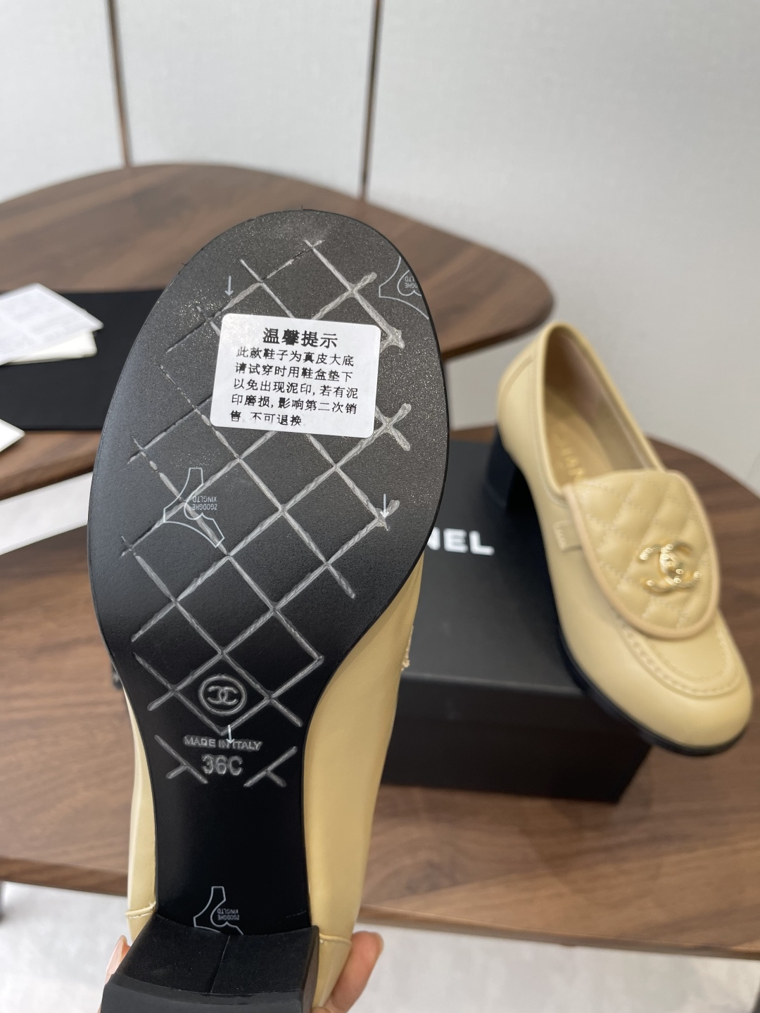 A pair of Chanel beige leather loafers with quilted gold CC logo displayed on a black shoe box. - Hình 9