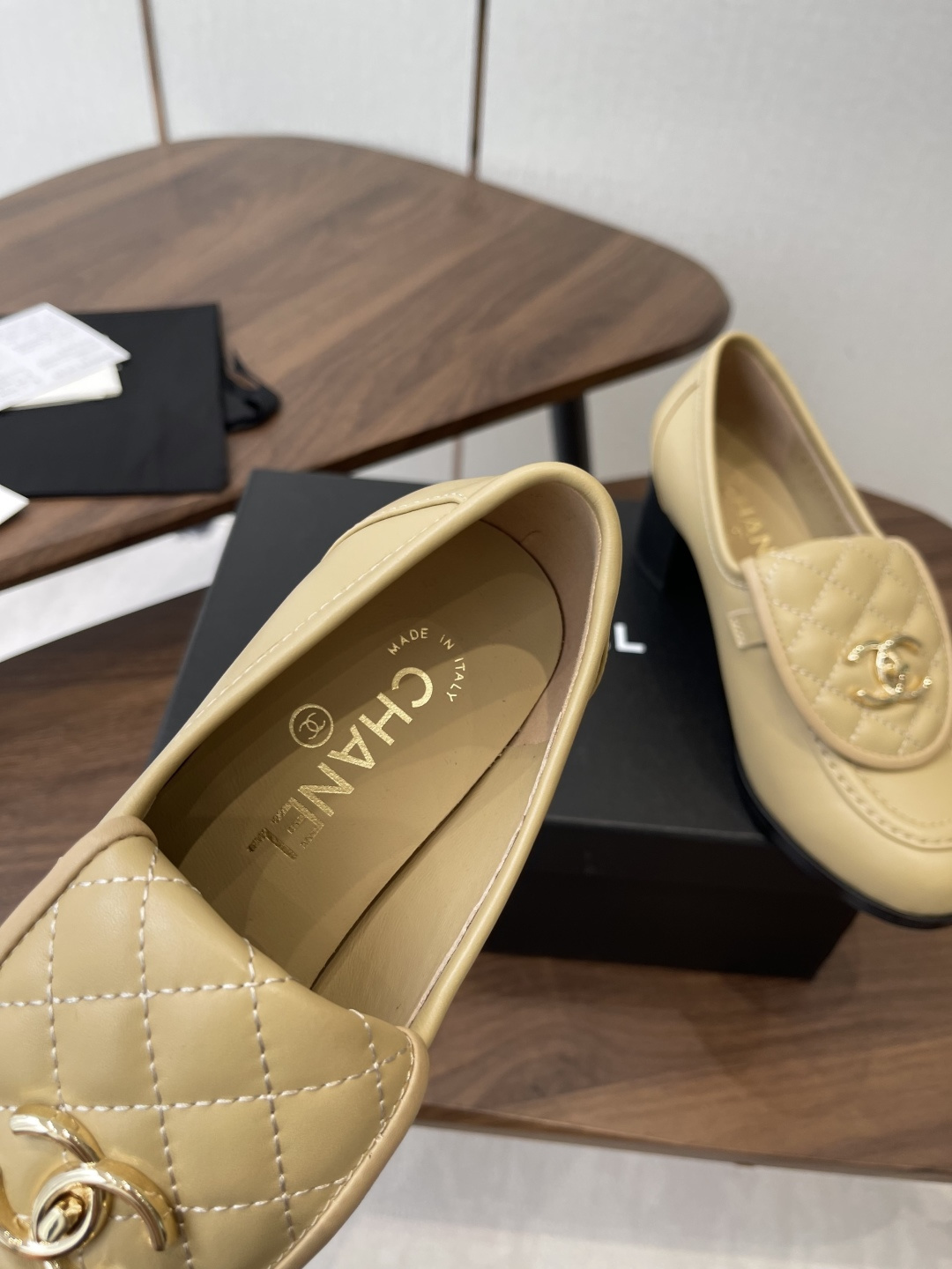 A pair of Chanel beige leather loafers with quilted gold CC logo displayed on a black shoe box. - Hình 7
