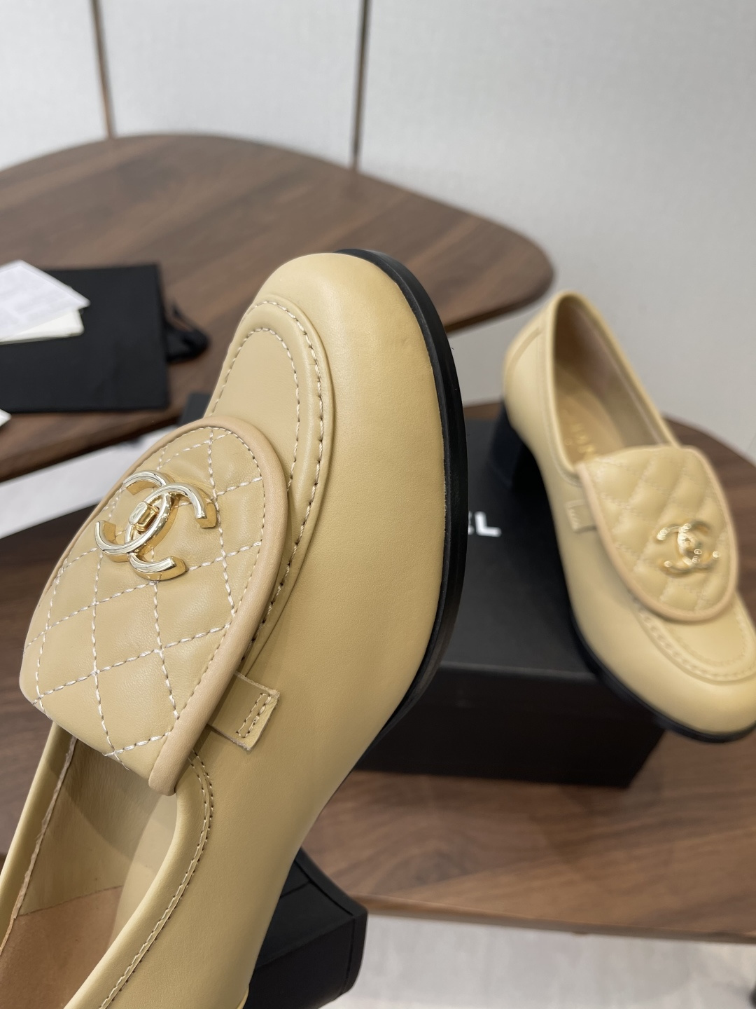 A pair of Chanel beige leather loafers with quilted gold CC logo displayed on a black shoe box. - Hình 6