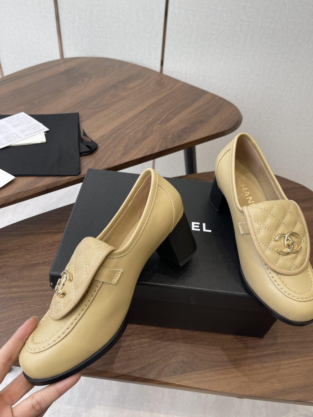 A pair of Chanel beige leather loafers with quilted gold CC logo displayed on a black shoe box. - Hình 5