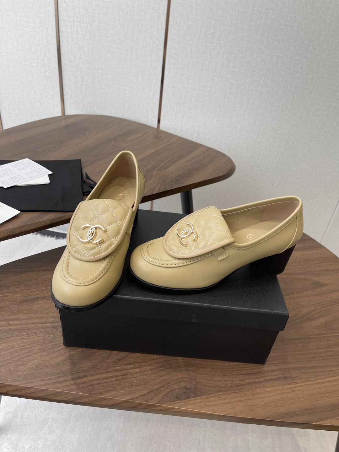 A pair of Chanel beige leather loafers with quilted gold CC logo displayed on a black shoe box. - Hình 3