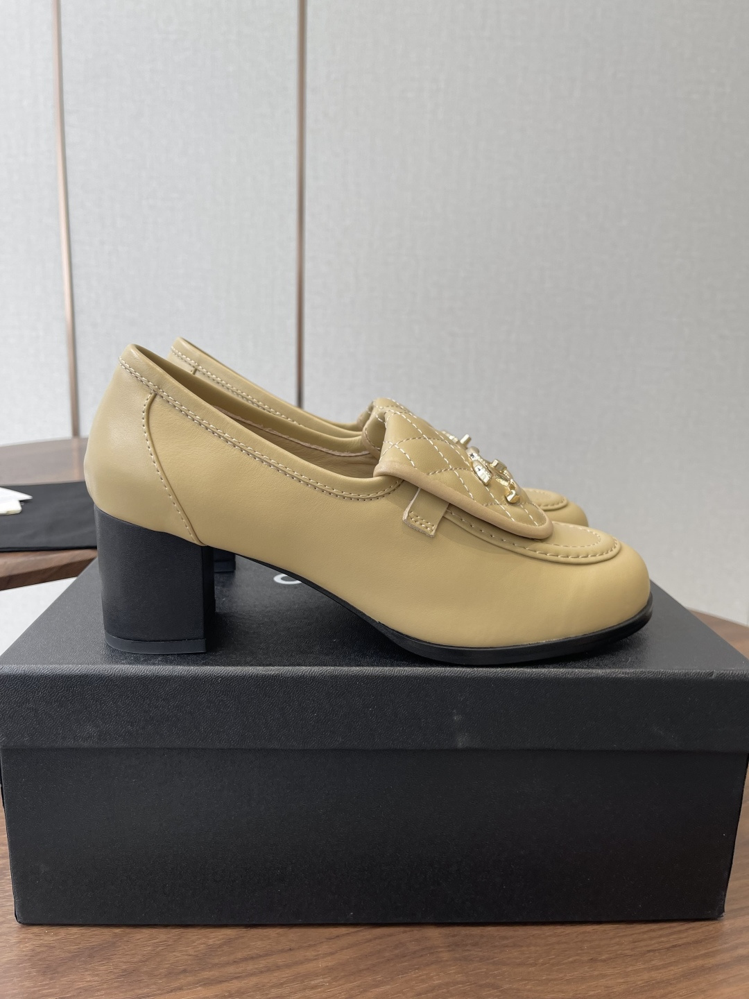 A pair of Chanel beige leather loafers with quilted gold CC logo displayed on a black shoe box. - Hình 2