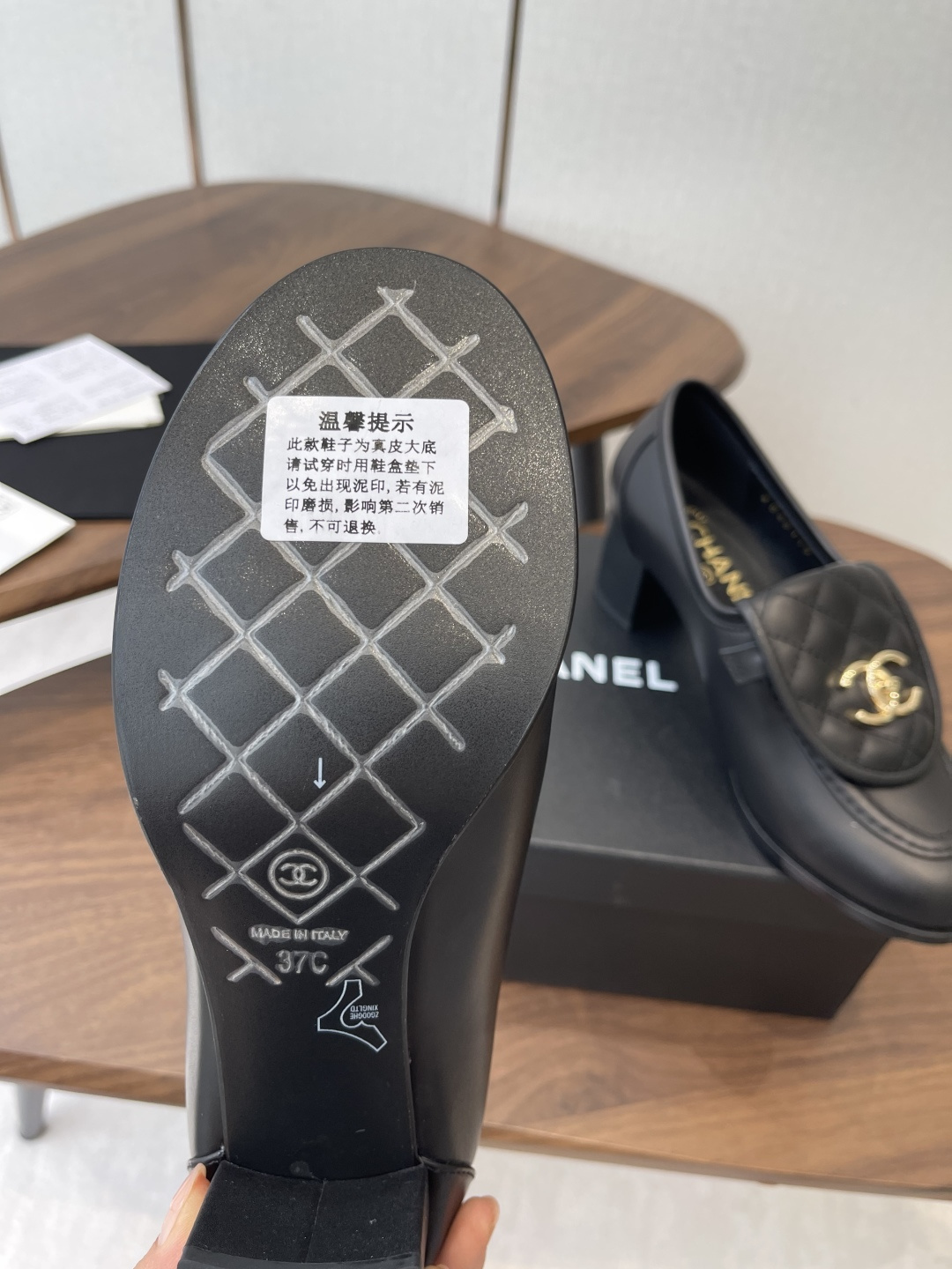 Elegant black leather loafers with quilted front flap and gold interlocking logo on a designer shoe box - Hình 9