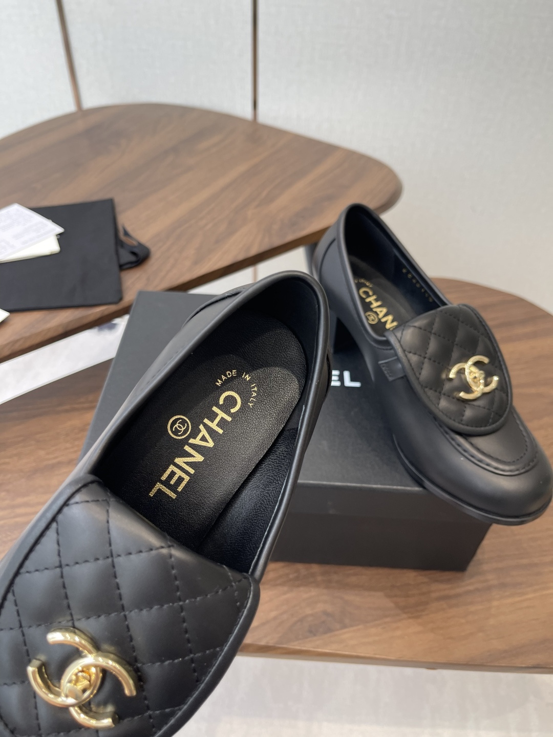 Elegant black leather loafers with quilted front flap and gold interlocking logo on a designer shoe box - Hình 7
