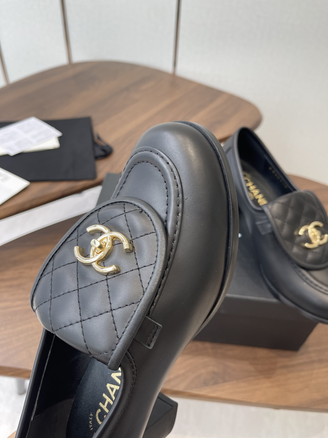 Elegant black leather loafers with quilted front flap and gold interlocking logo on a designer shoe box - Hình 6