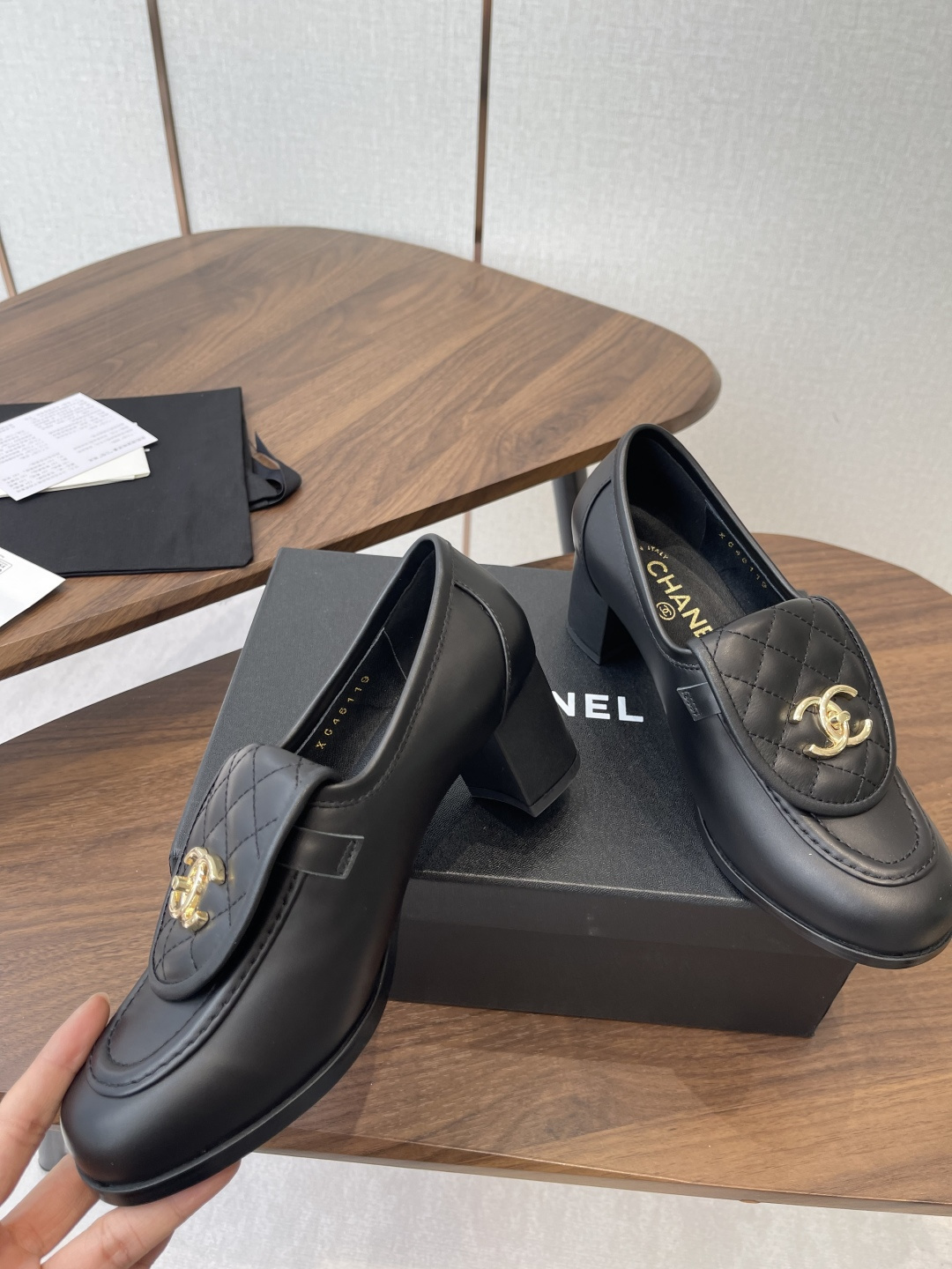 Elegant black leather loafers with quilted front flap and gold interlocking logo on a designer shoe box - Hình 5
