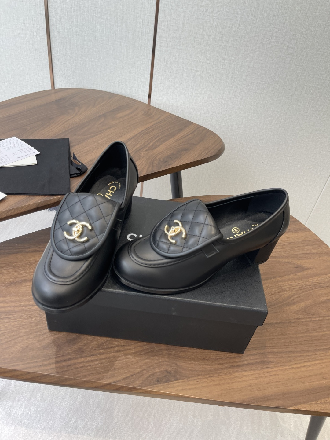 Elegant black leather loafers with quilted front flap and gold interlocking logo on a designer shoe box - Hình 4