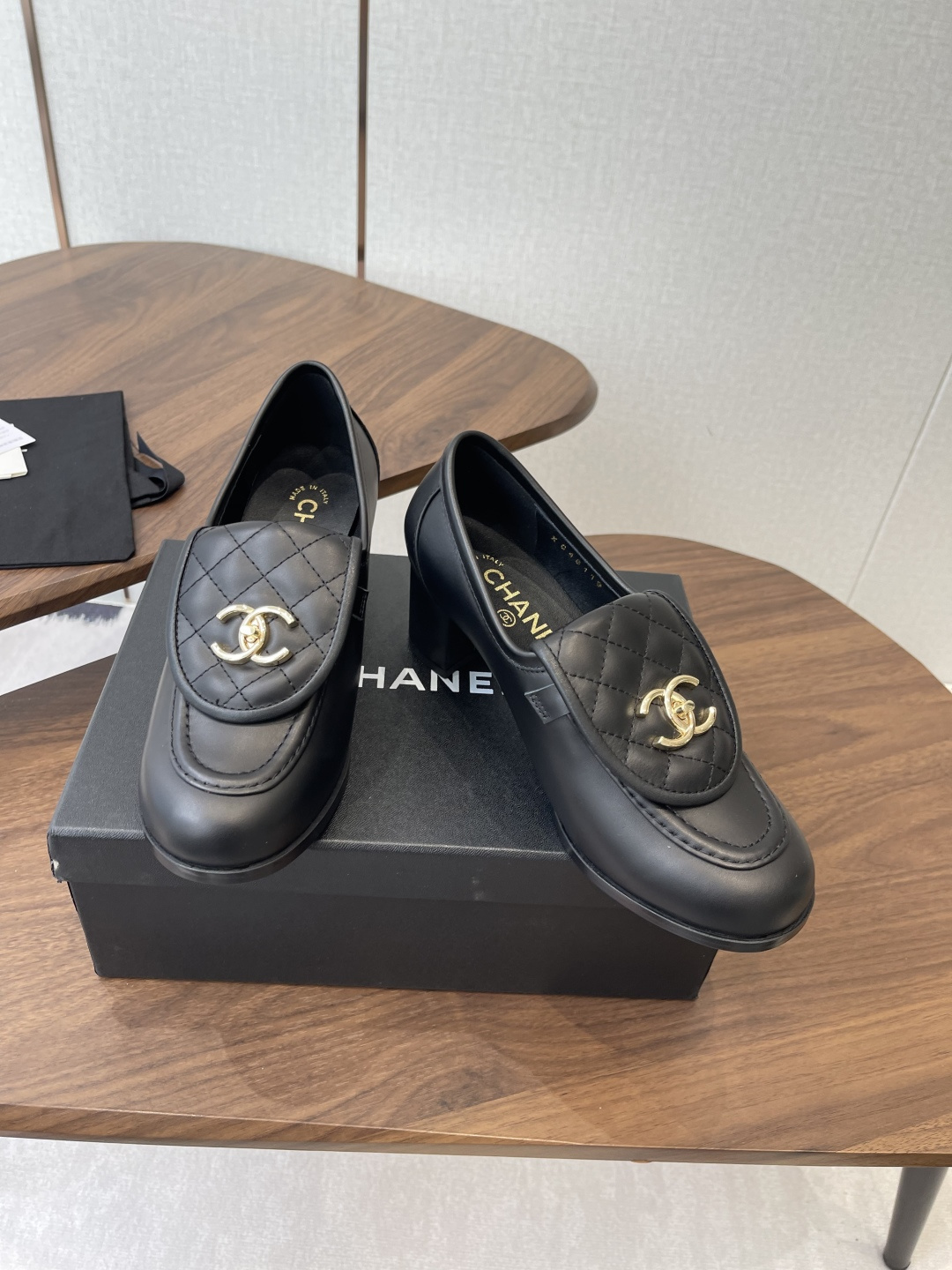 Elegant black leather loafers with quilted front flap and gold interlocking logo on a designer shoe box - Hình 3