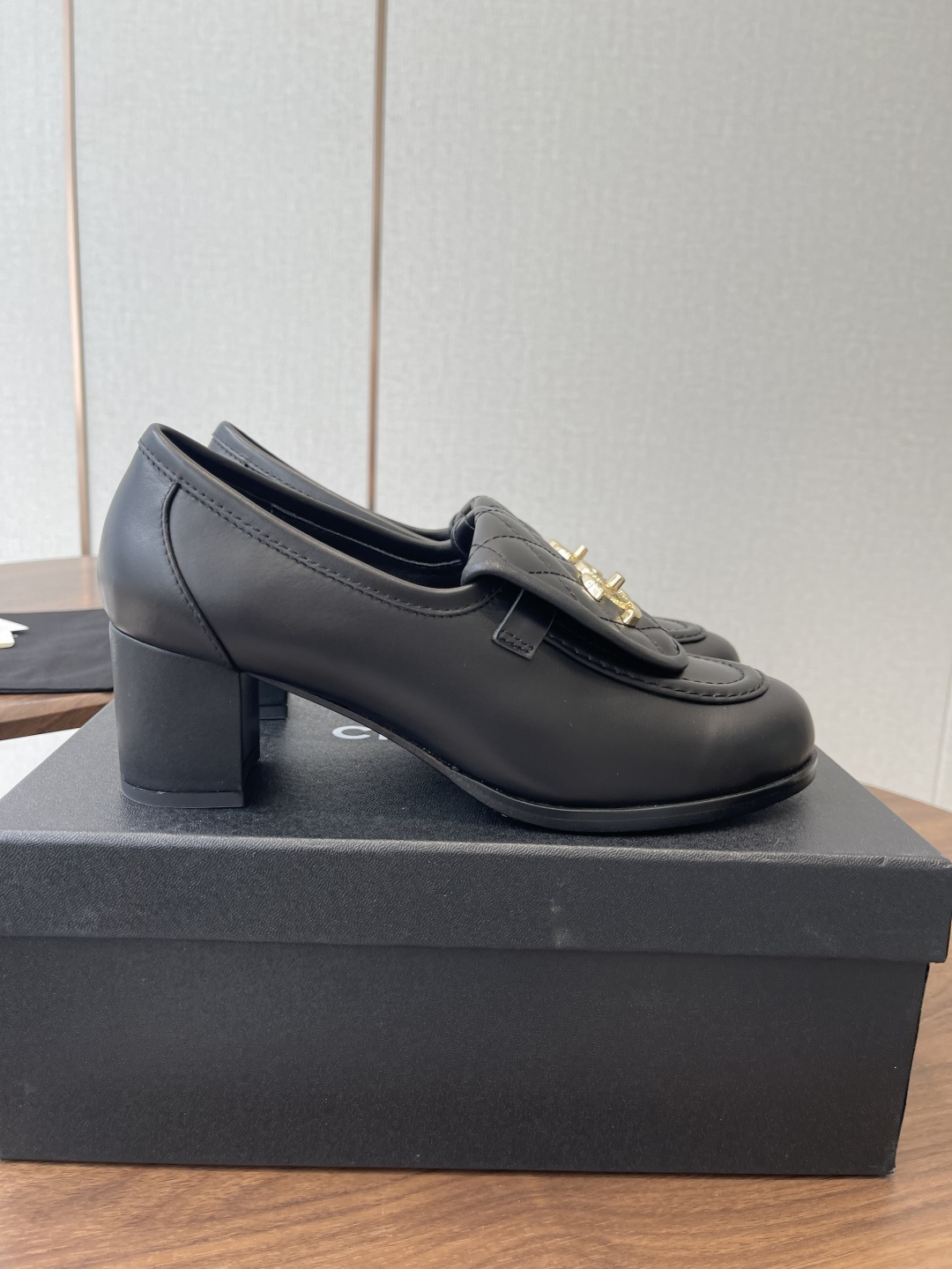 Elegant black leather loafers with quilted front flap and gold interlocking logo on a designer shoe box - Hình 2