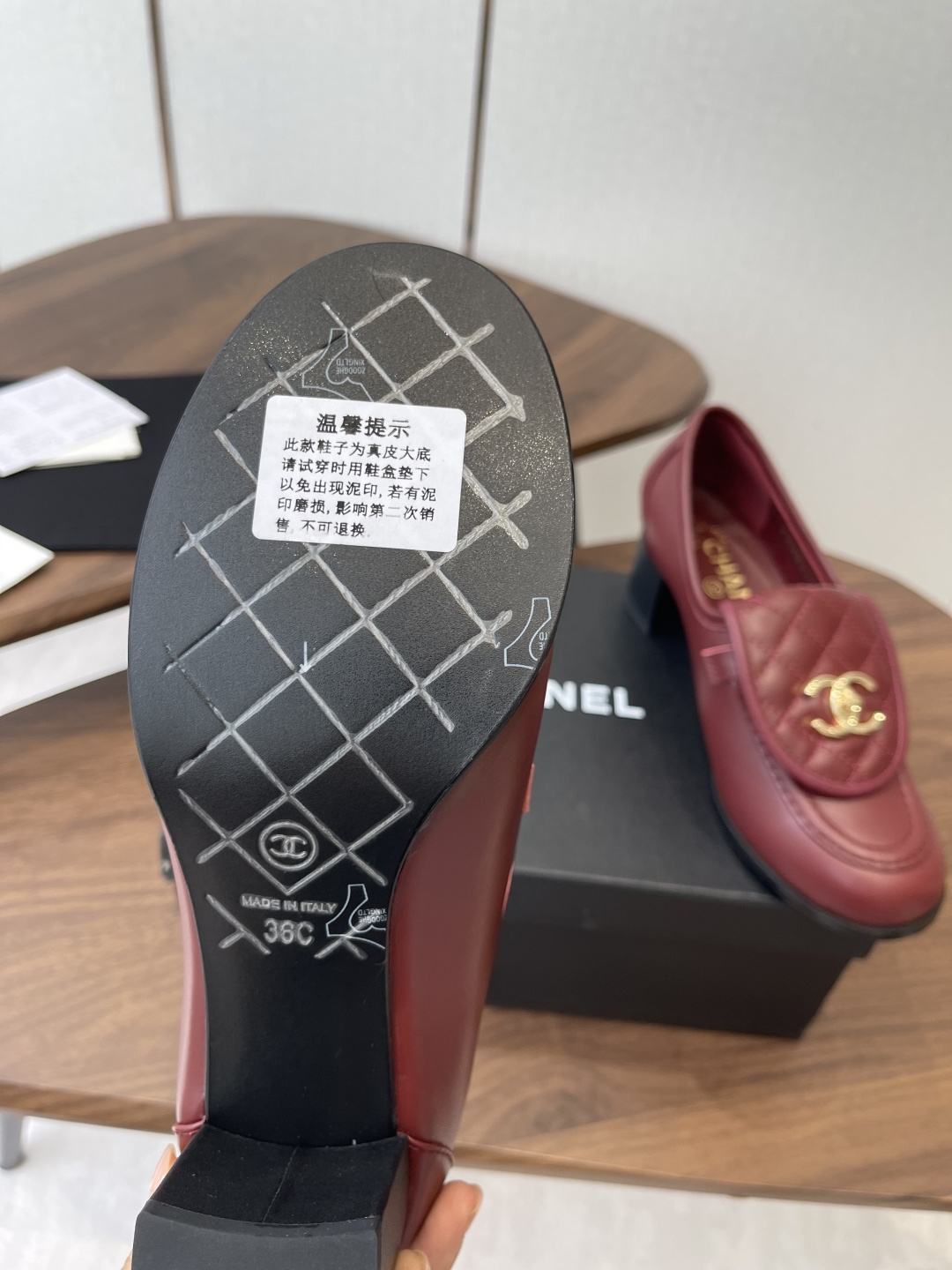 A pair of luxury burgundy Chanel quilted leather loafers with gold CC logos displayed on a black shoe box. - Hình 9