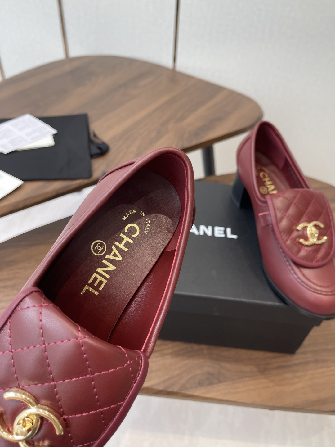 A pair of luxury burgundy Chanel quilted leather loafers with gold CC logos displayed on a black shoe box. - Hình 7