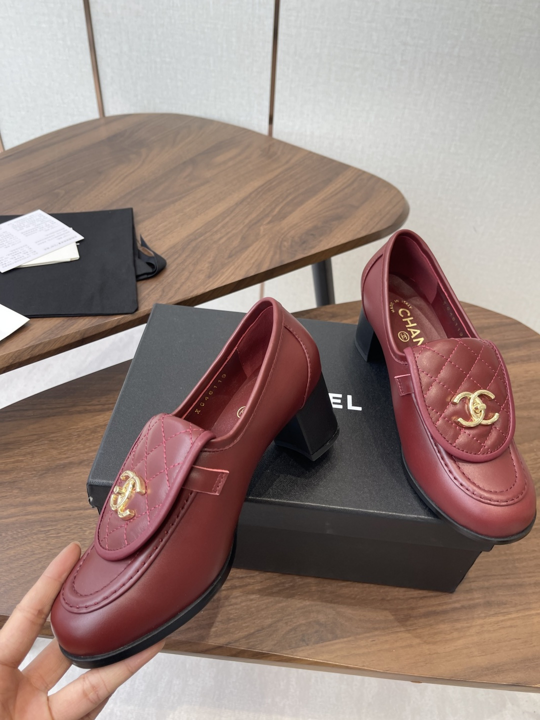 A pair of luxury burgundy Chanel quilted leather loafers with gold CC logos displayed on a black shoe box. - Hình 5