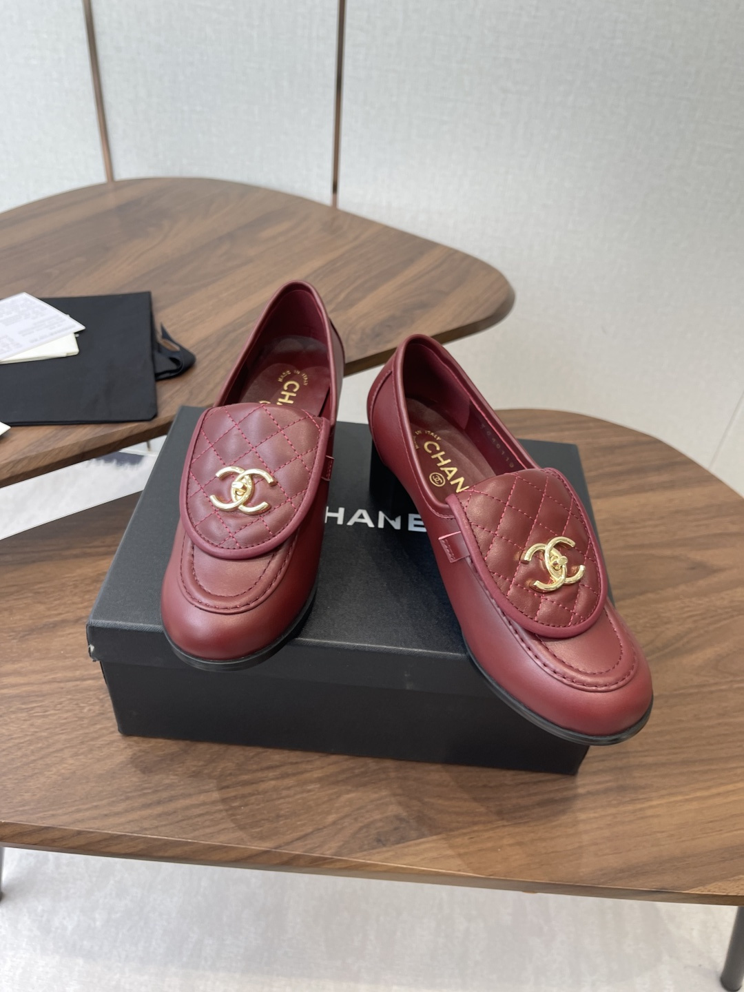 A pair of luxury burgundy Chanel quilted leather loafers with gold CC logos displayed on a black shoe box. - Hình 3
