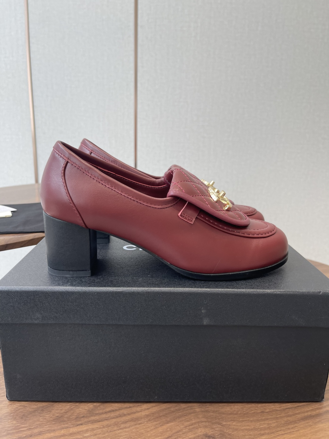 A pair of luxury burgundy Chanel quilted leather loafers with gold CC logos displayed on a black shoe box. - Hình 2