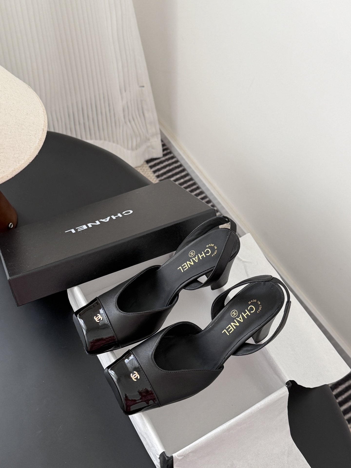 Pair of black Chanel leather slingback pumps with patent cap toe and gold CC logo displayed with a designer box. - Hình 9