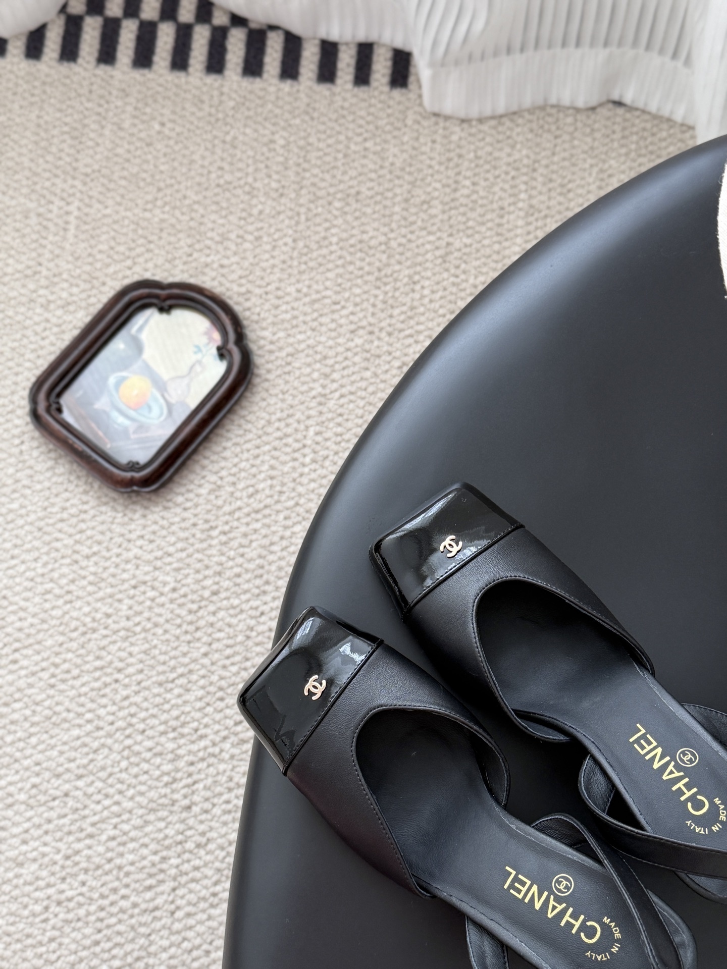 Pair of black Chanel leather slingback pumps with patent cap toe and gold CC logo displayed with a designer box. - Hình 7