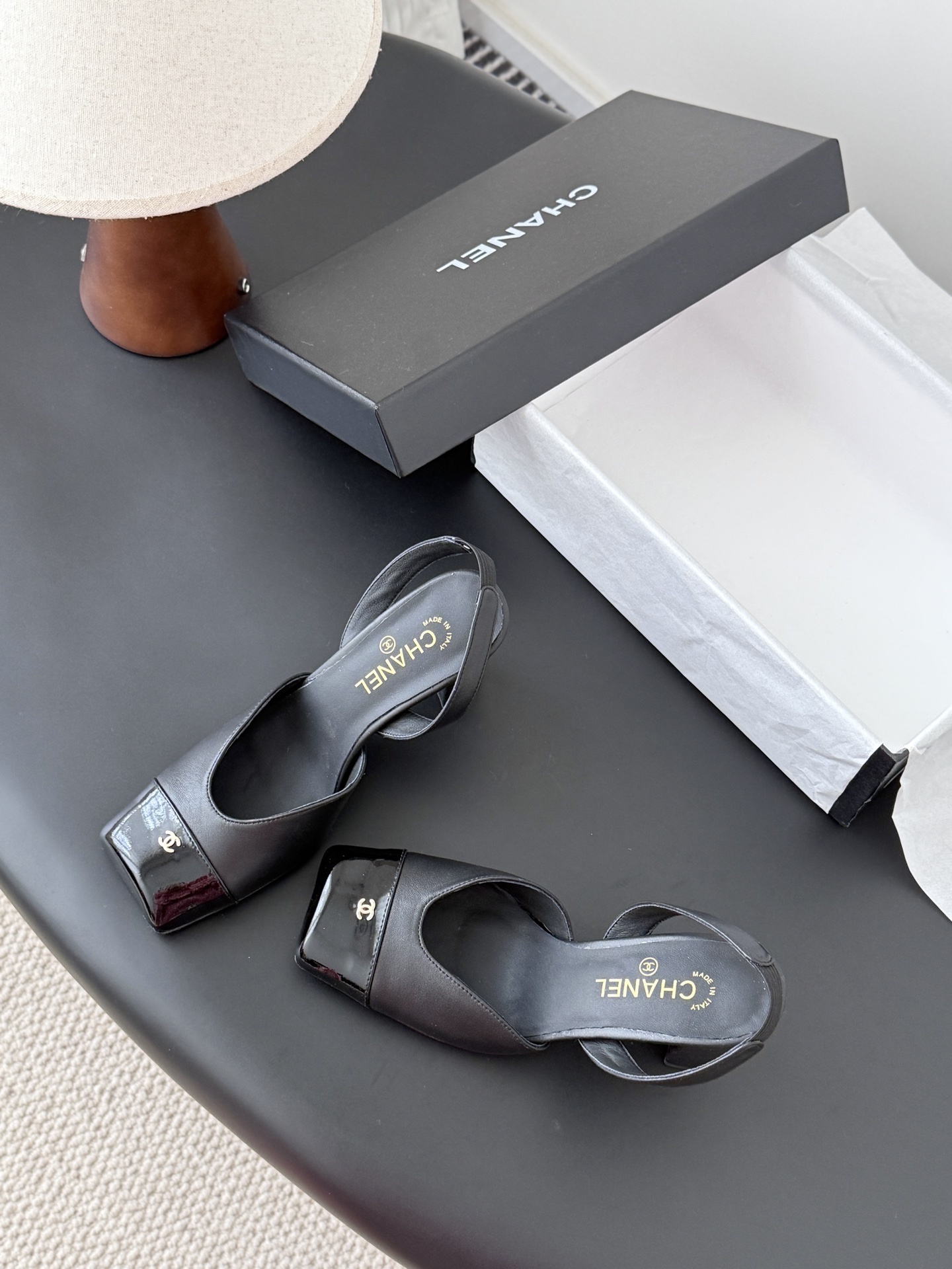 Pair of black Chanel leather slingback pumps with patent cap toe and gold CC logo displayed with a designer box. - Hình 6