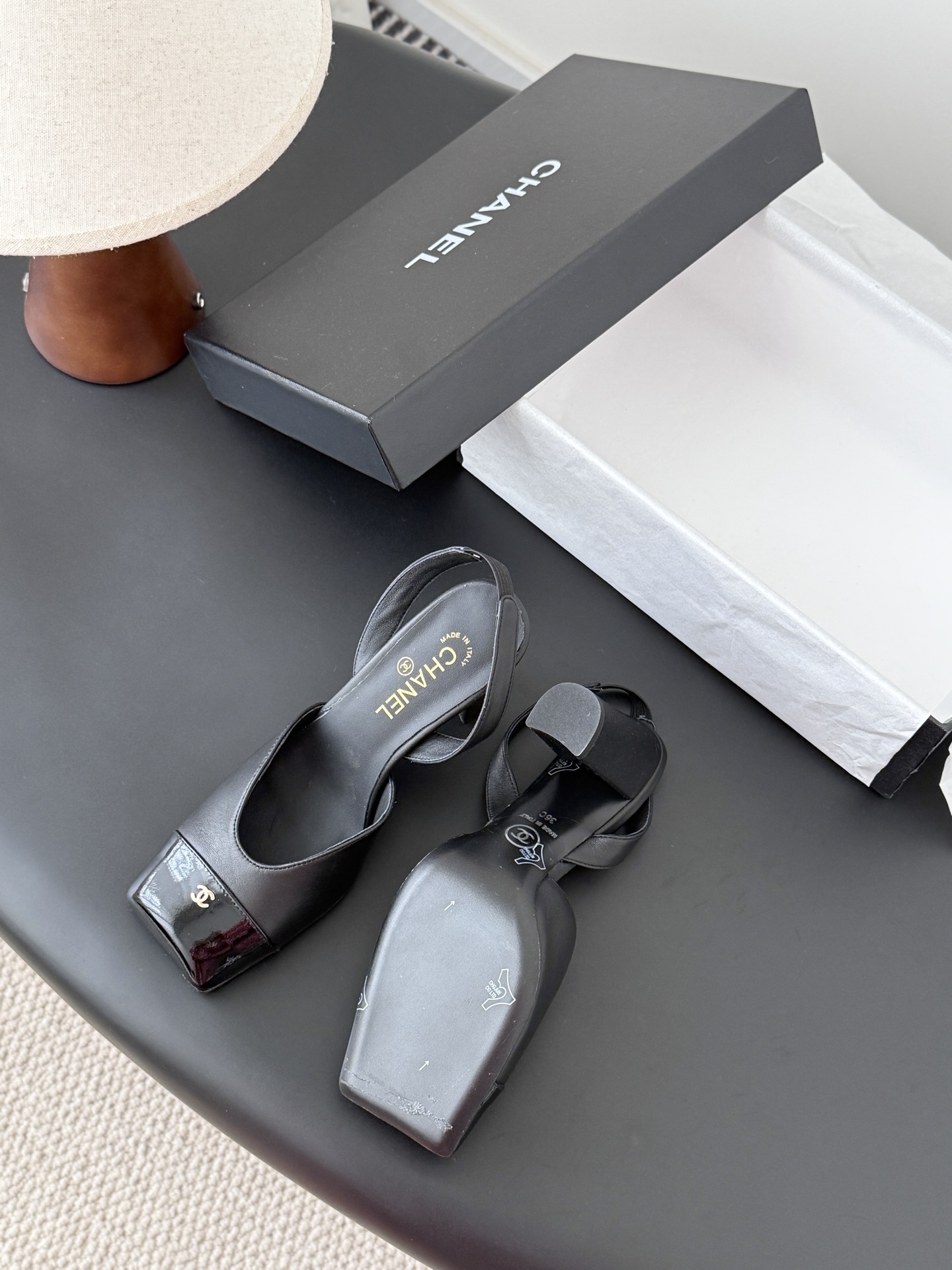 Pair of black Chanel leather slingback pumps with patent cap toe and gold CC logo displayed with a designer box. - Hình 5