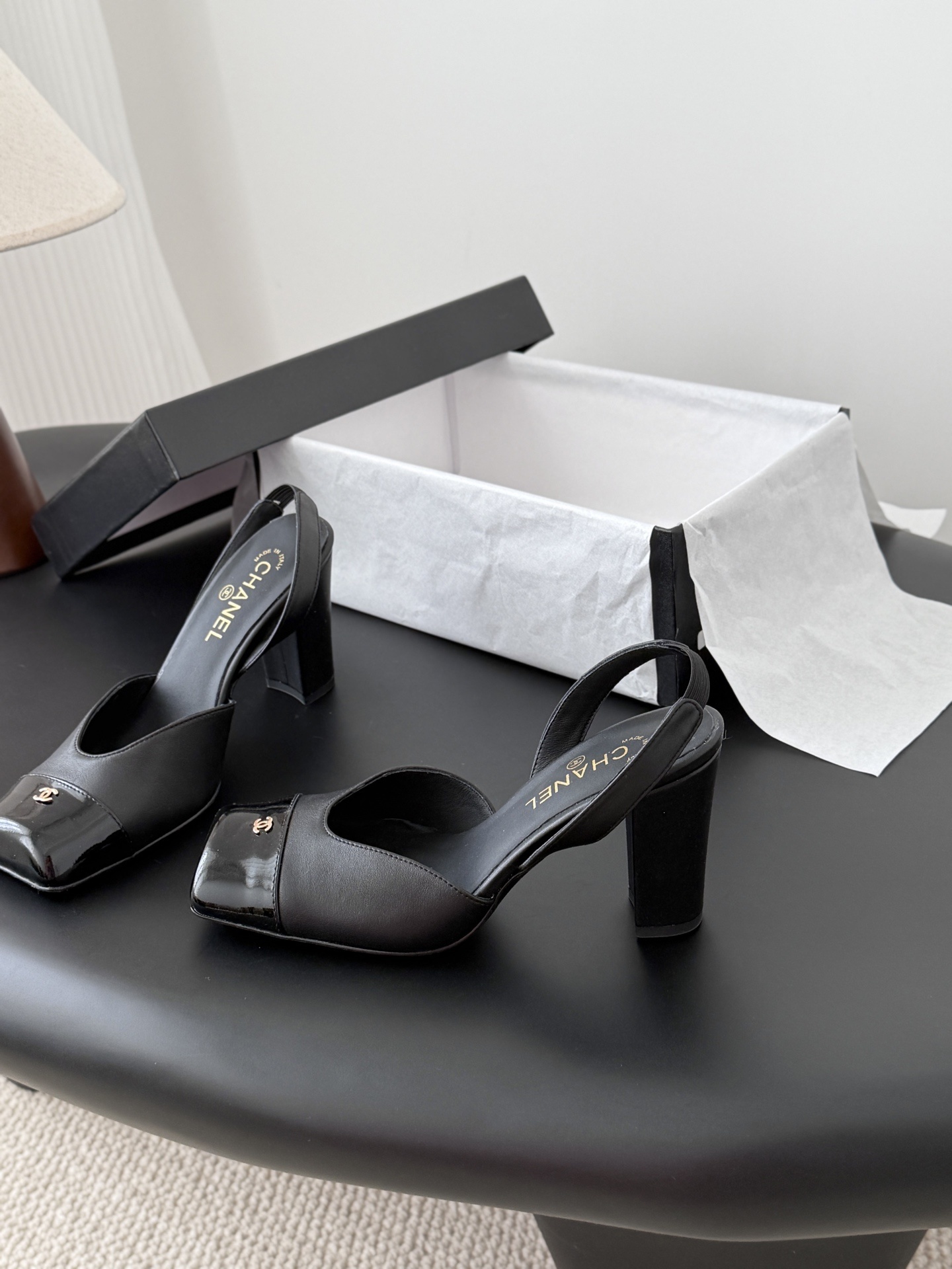 Pair of black Chanel leather slingback pumps with patent cap toe and gold CC logo displayed with a designer box. - Hình 2